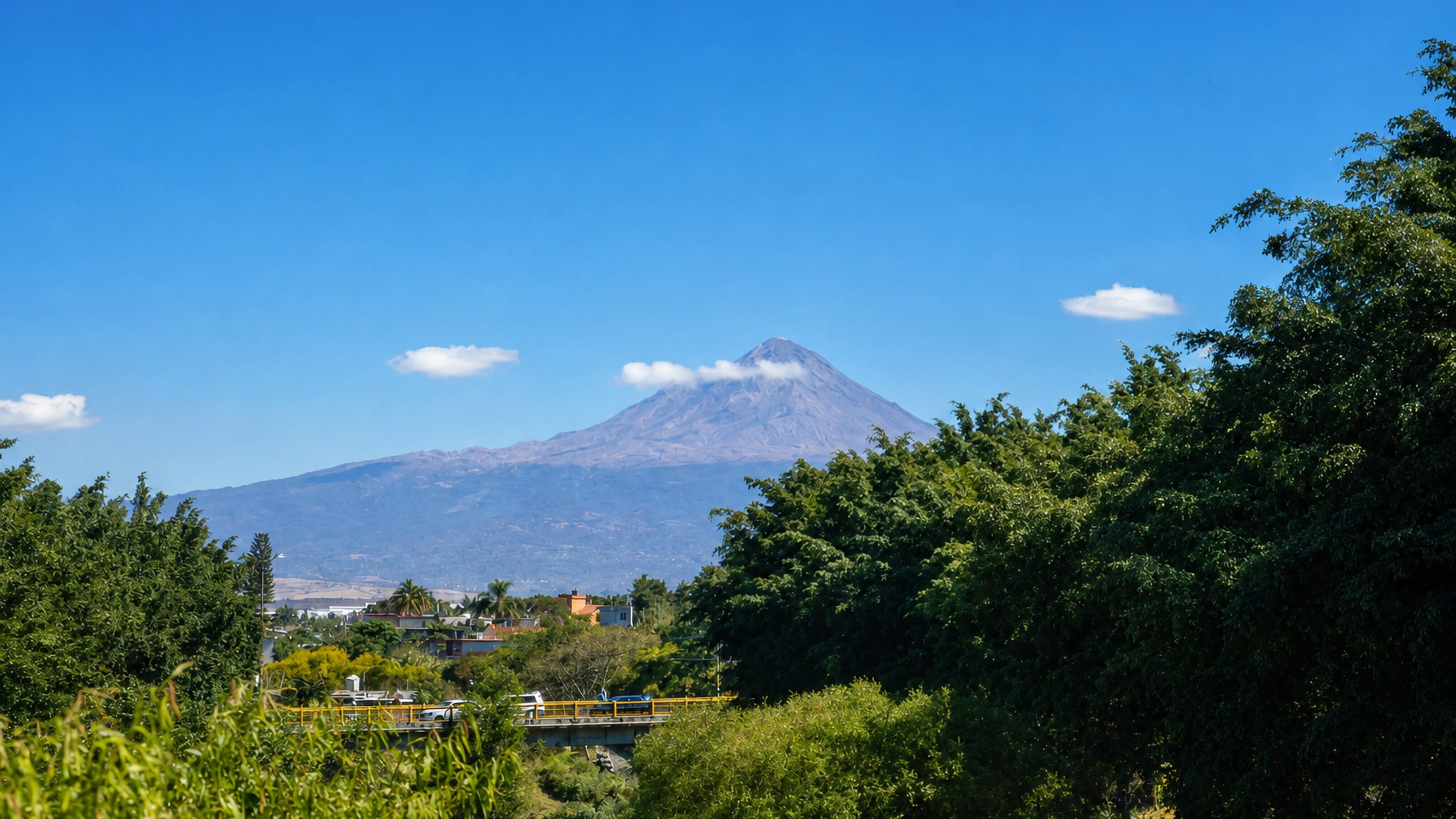 A volcanic peak rising beyond treetops and low rooftops on the edge of Cuautla, Morelos, Mexico.