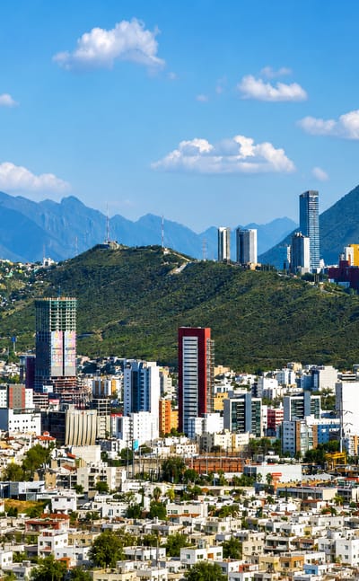 Monterrey's high-rise skyline set against the rugged Sierra Madre mountains under a bright blue sky.
