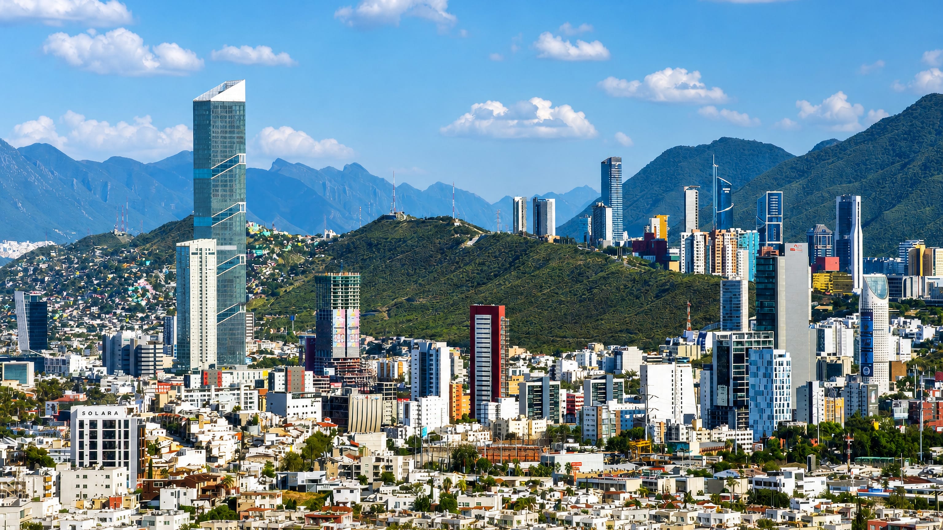 Monterrey's high-rise skyline set against the rugged Sierra Madre mountains under a bright blue sky.