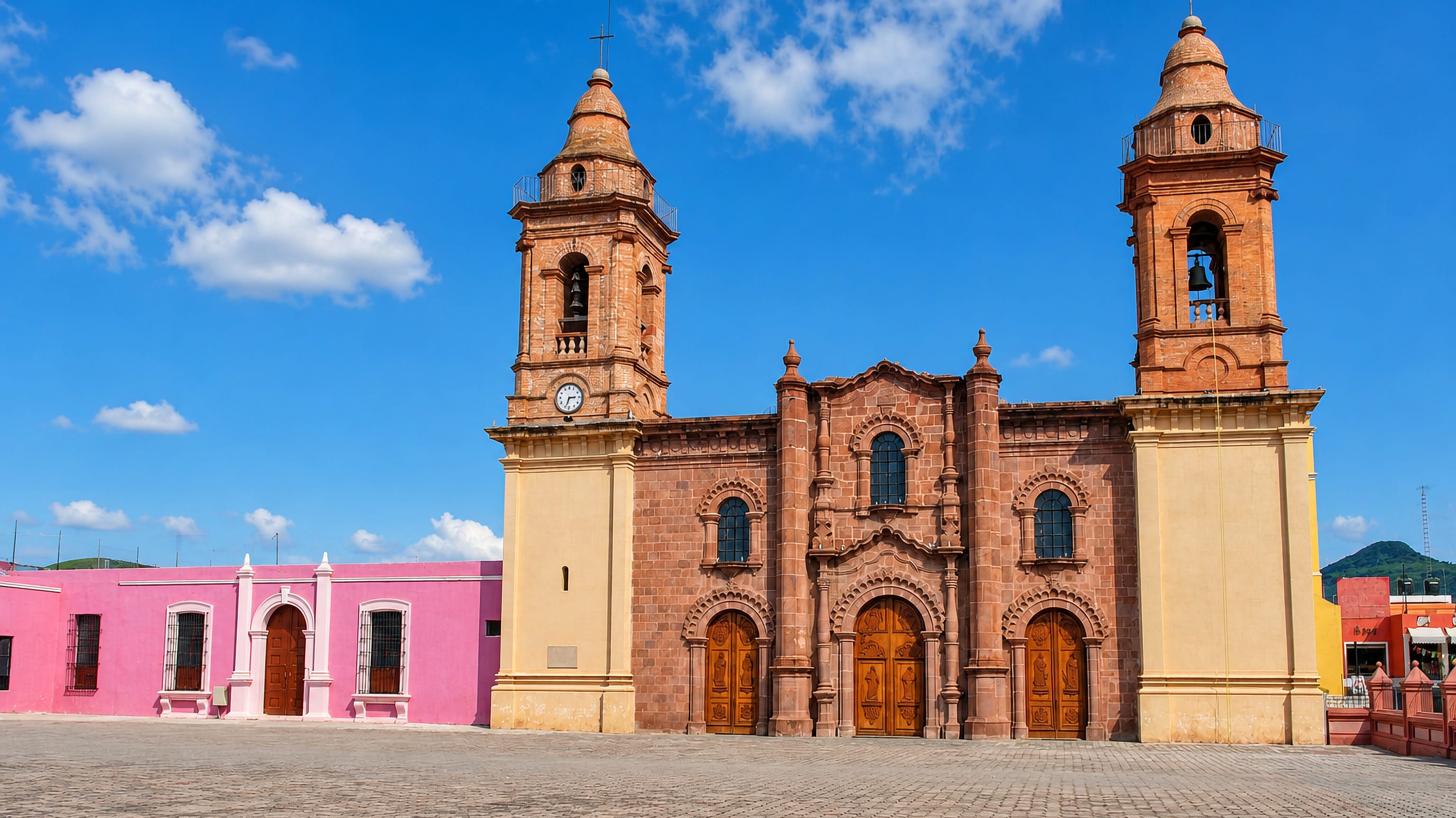 Twin-towered stone cathedral of Ciudad de Huajuapan de León facing a cobbled plaza with pink colonial buildings