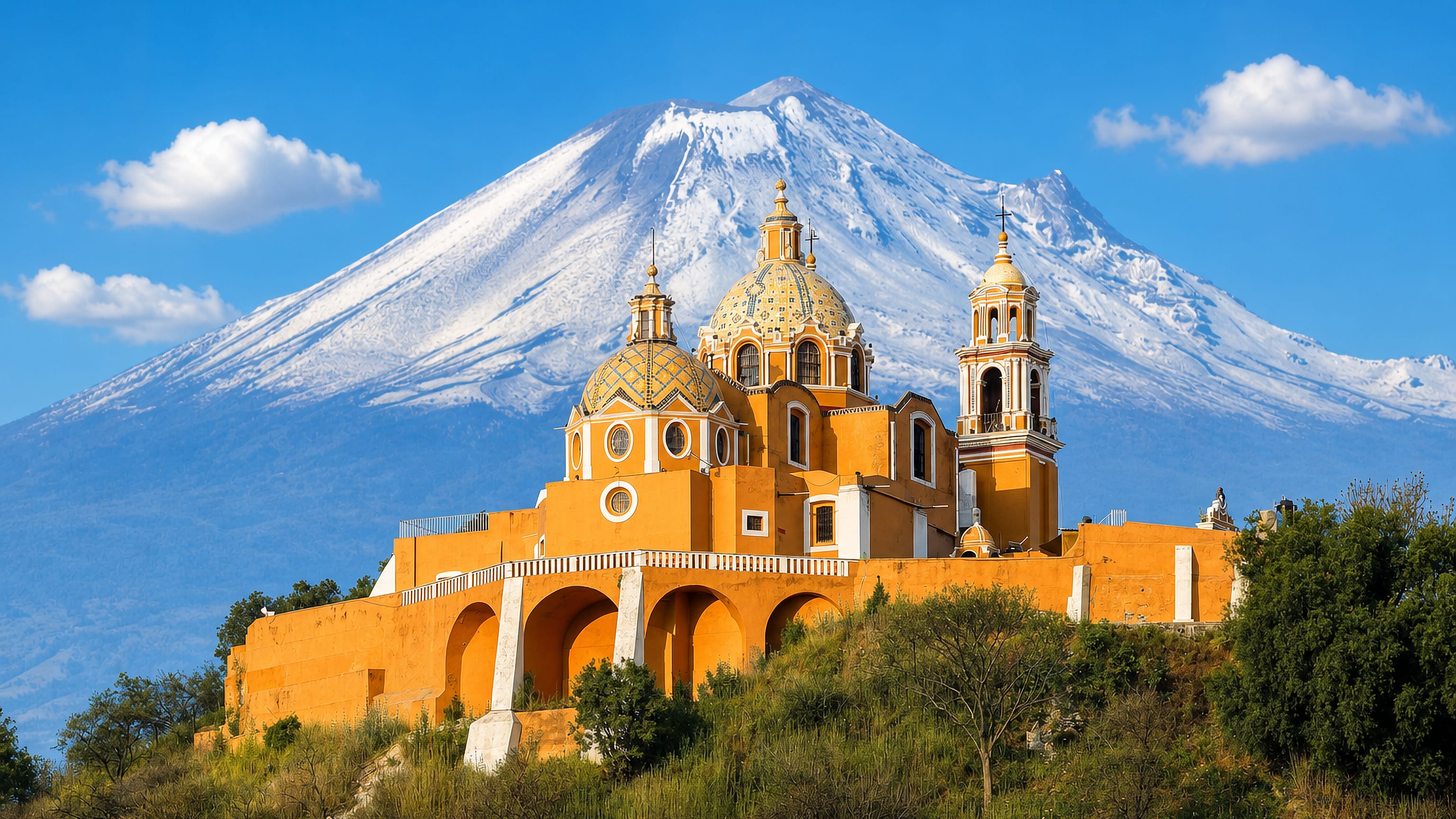 Cholula's yellow hilltop Church of Our Lady of Remedies with the snow-capped Popocatepetl volcano behind.