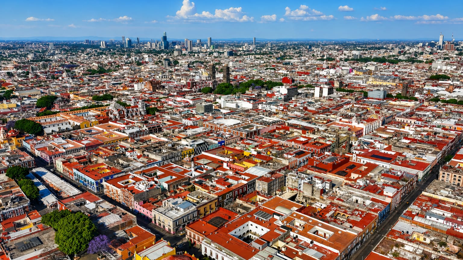 Aerial view of Puebla's colonial centre, red-tiled rooftops and cathedral towers with distant skyscrapers.