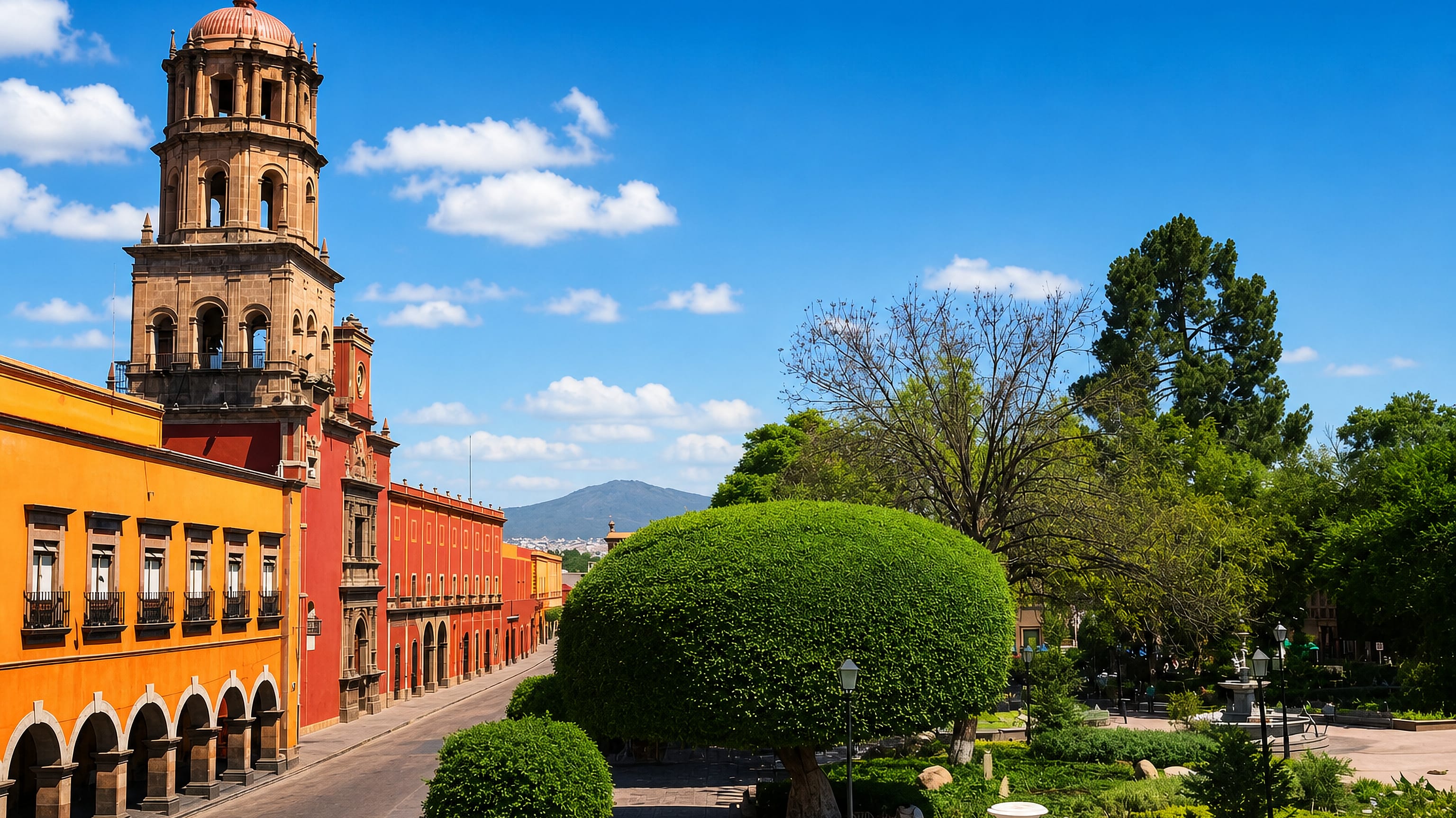 Baroque bell tower rising above ochre and red colonial arcades beside a leafy plaza in Santiago de Queretaro.