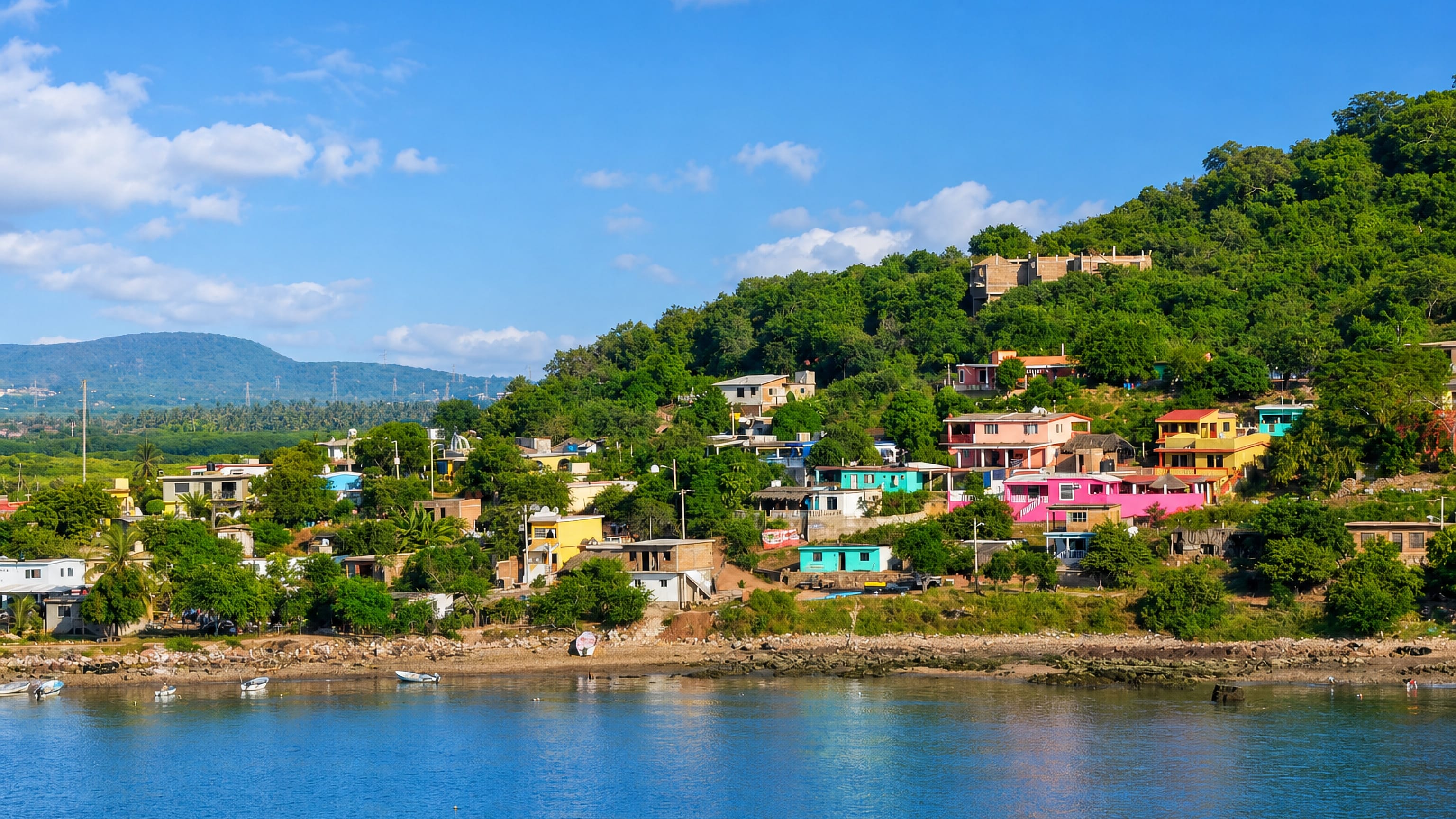 Brightly painted hillside houses above a calm bay on the wooded coast near Mazatlán, Sinaloa.