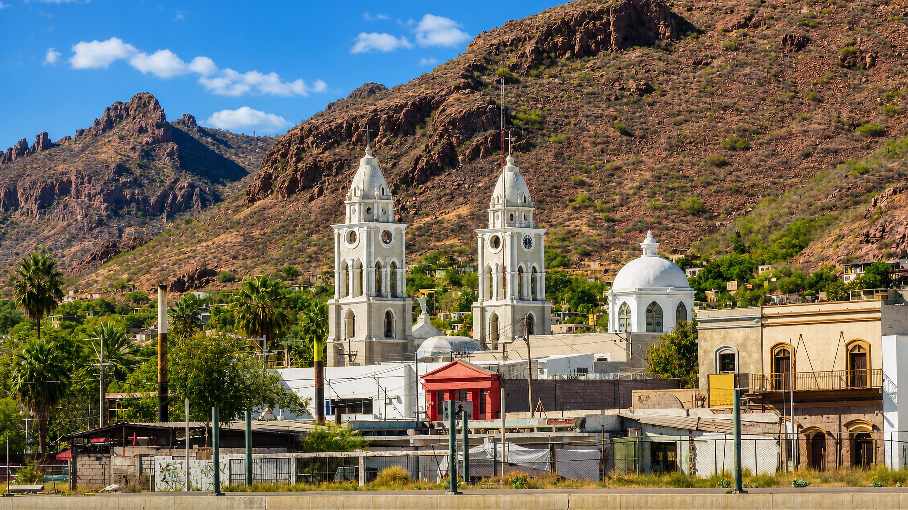 Twin-towered white church in Heroica Guaymas, Mexico, below arid rocky hills above the harbour front.