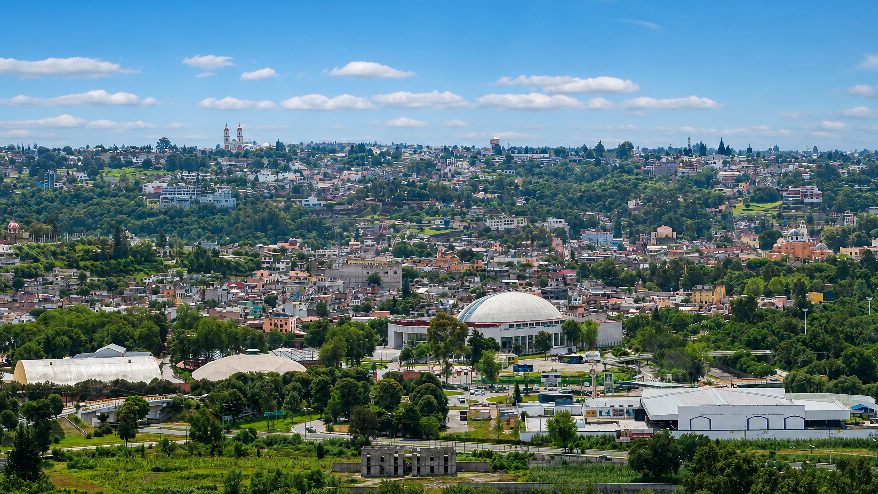 Tlaxcala, Mexico, spread across green hills, with a white domed arena and hilltop church towers on the skyline.