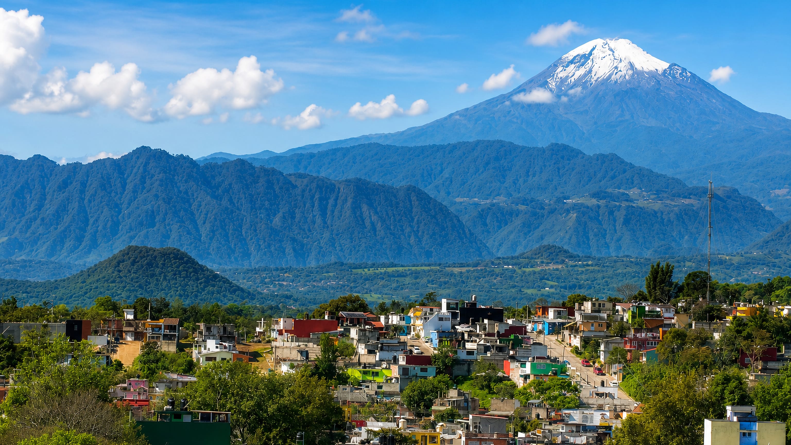 Colorful hillside houses of Xalapa with the snow-capped Pico de Orizaba volcano rising behind.