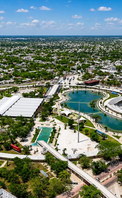 Aerial view of a modern oval-lagoon park with ring paths in Merida, Yucatan, low-rise city beyond.