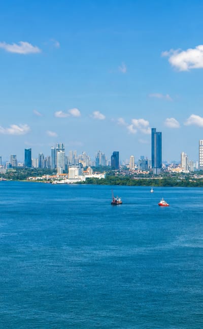 Johor Bahru's high-rise skyline across the Straits of Johor with boats on the blue water