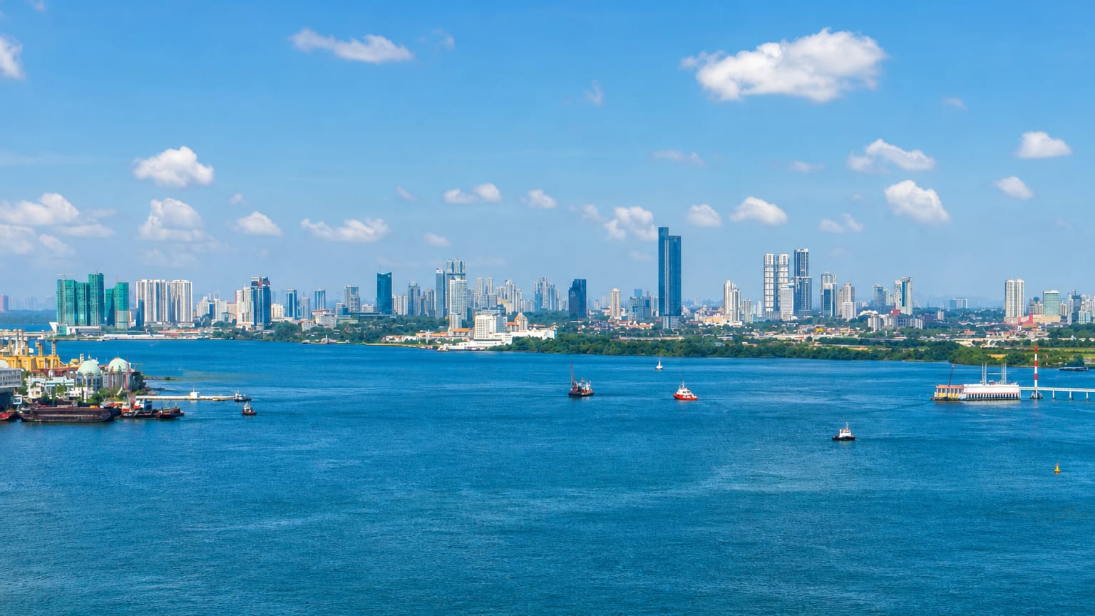 Johor Bahru's high-rise skyline across the Straits of Johor with boats on the blue water