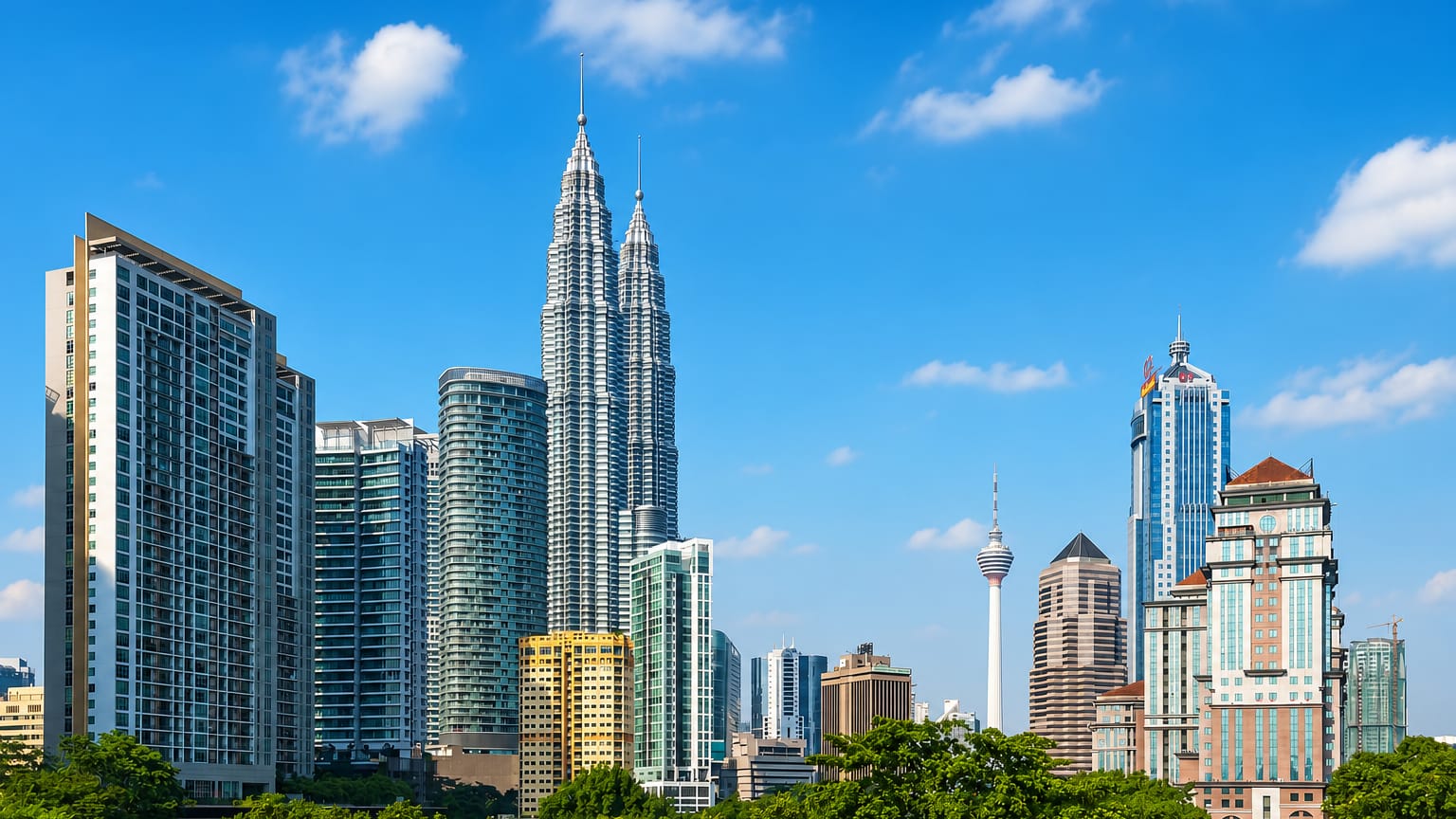 Kuala Lumpur skyline with the Petronas Twin Towers and KL Tower rising above green trees under a blue sky.