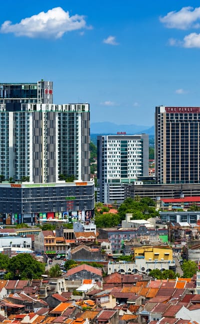 Malacca skyline with modern high-rise towers and a Ferris wheel rising above the red-roofed old town under blue sky.