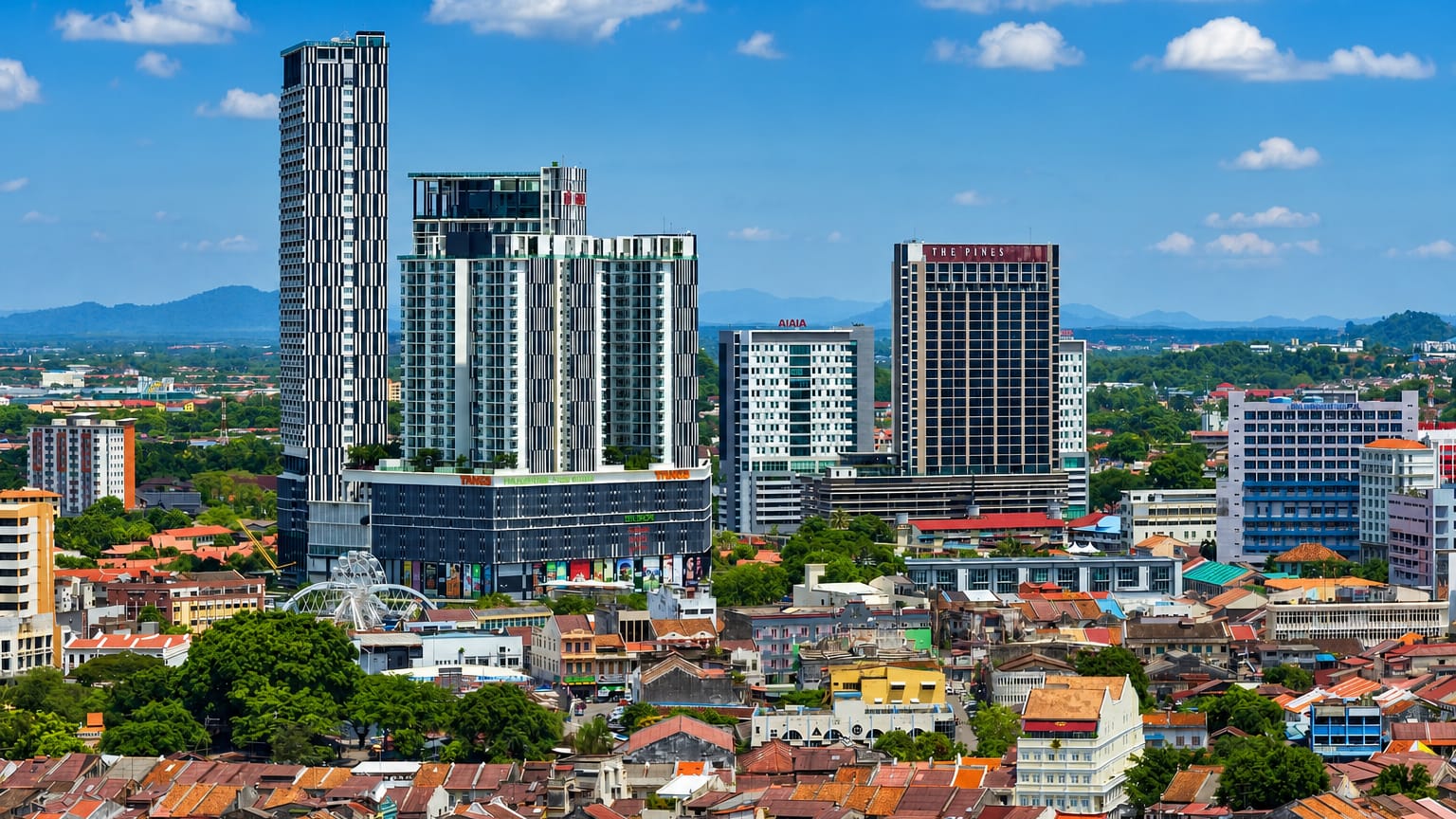 Malacca skyline with modern high-rise towers and a Ferris wheel rising above the red-roofed old town under blue sky.