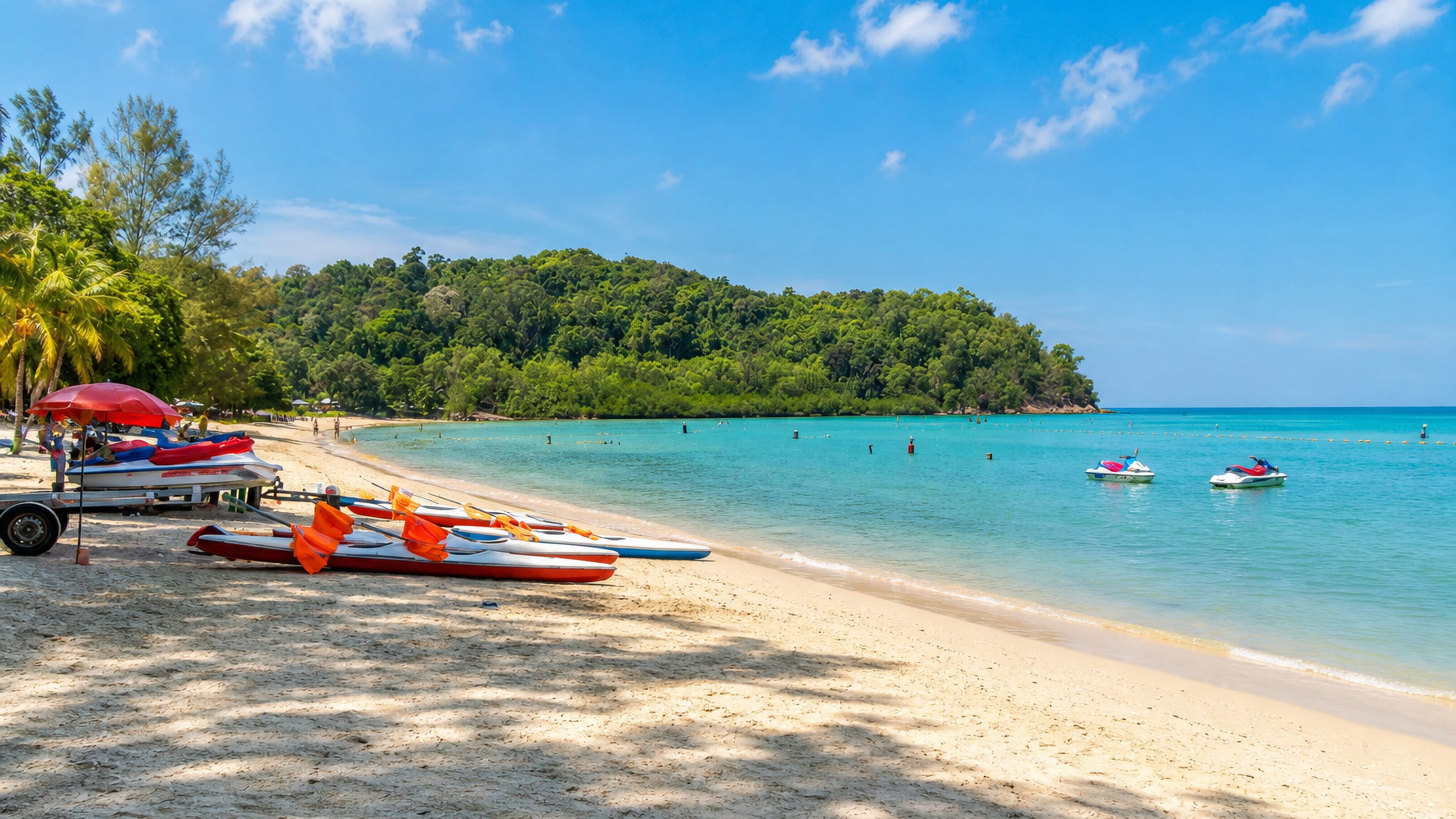 Sandy beach at Port Dickson, Malaysia, with kayaks and jet-skis on the shore and a forested cape across the bay.
