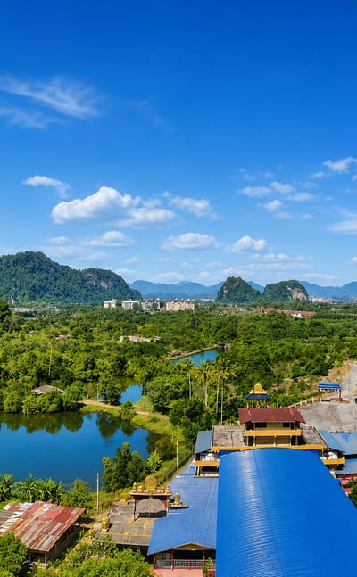 Limestone karst hills around Ipoh with a blue-roofed cave temple, palm groves and a still pond