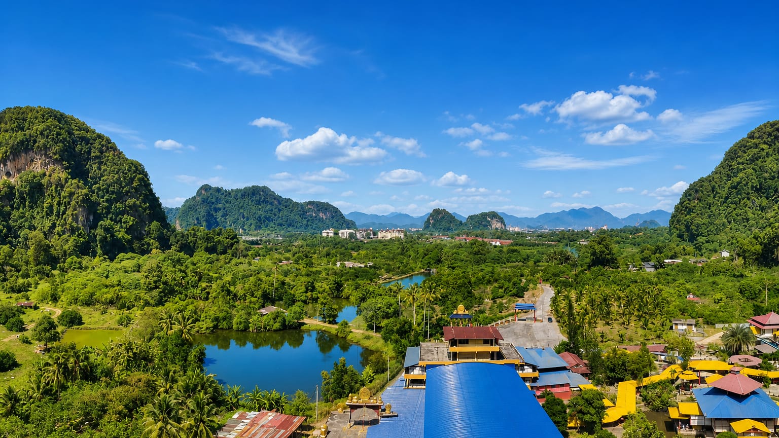 Limestone karst hills around Ipoh with a blue-roofed cave temple, palm groves and a still pond