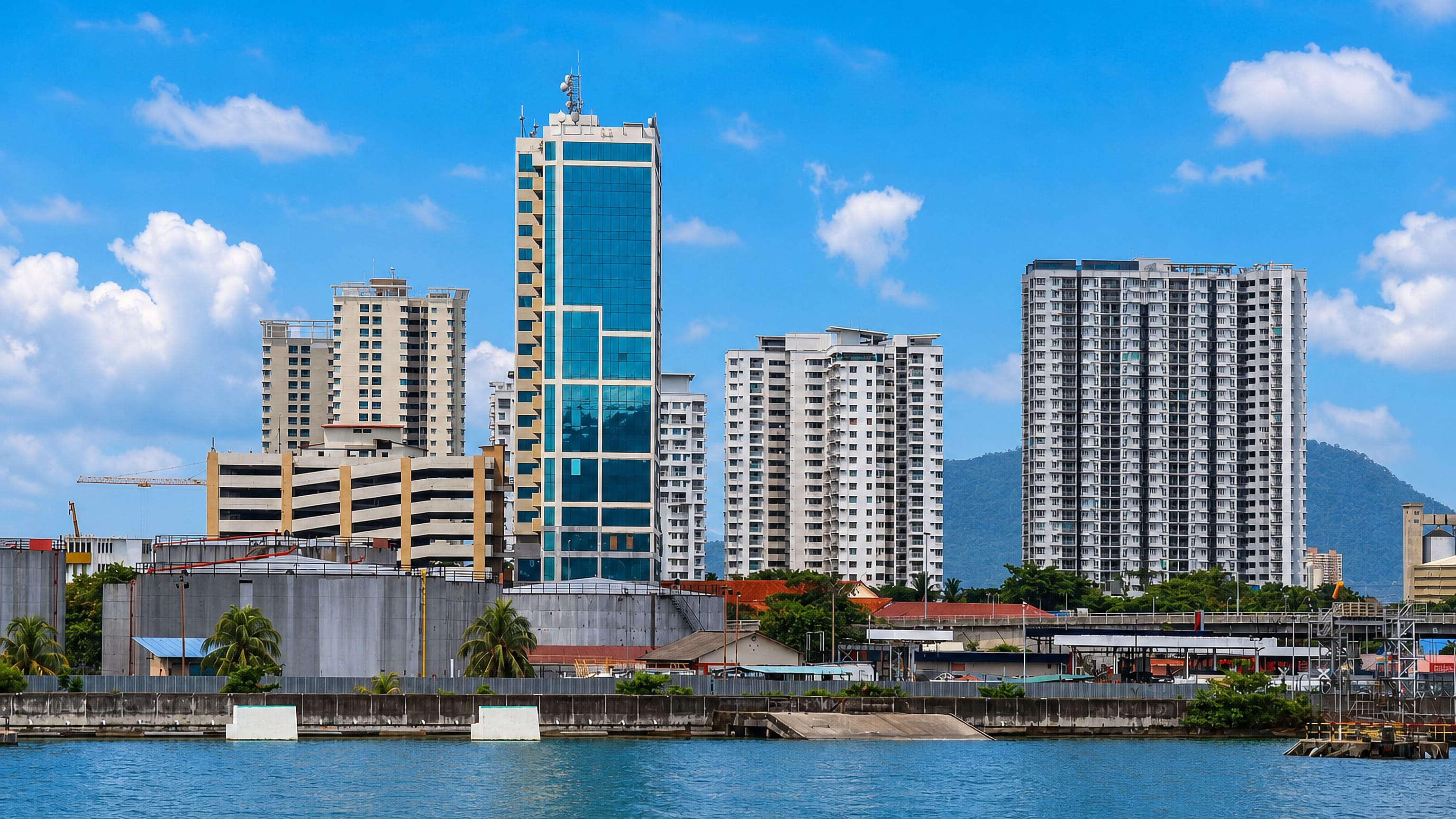 Butterworth, Malaysia, seen across the channel: a blue glass tower and high-rise flats below a green hill.