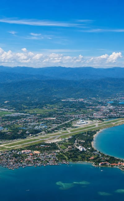 Aerial view of Kota Kinabalu's coastline, airport runway and city backed by the Crocker Range mountains