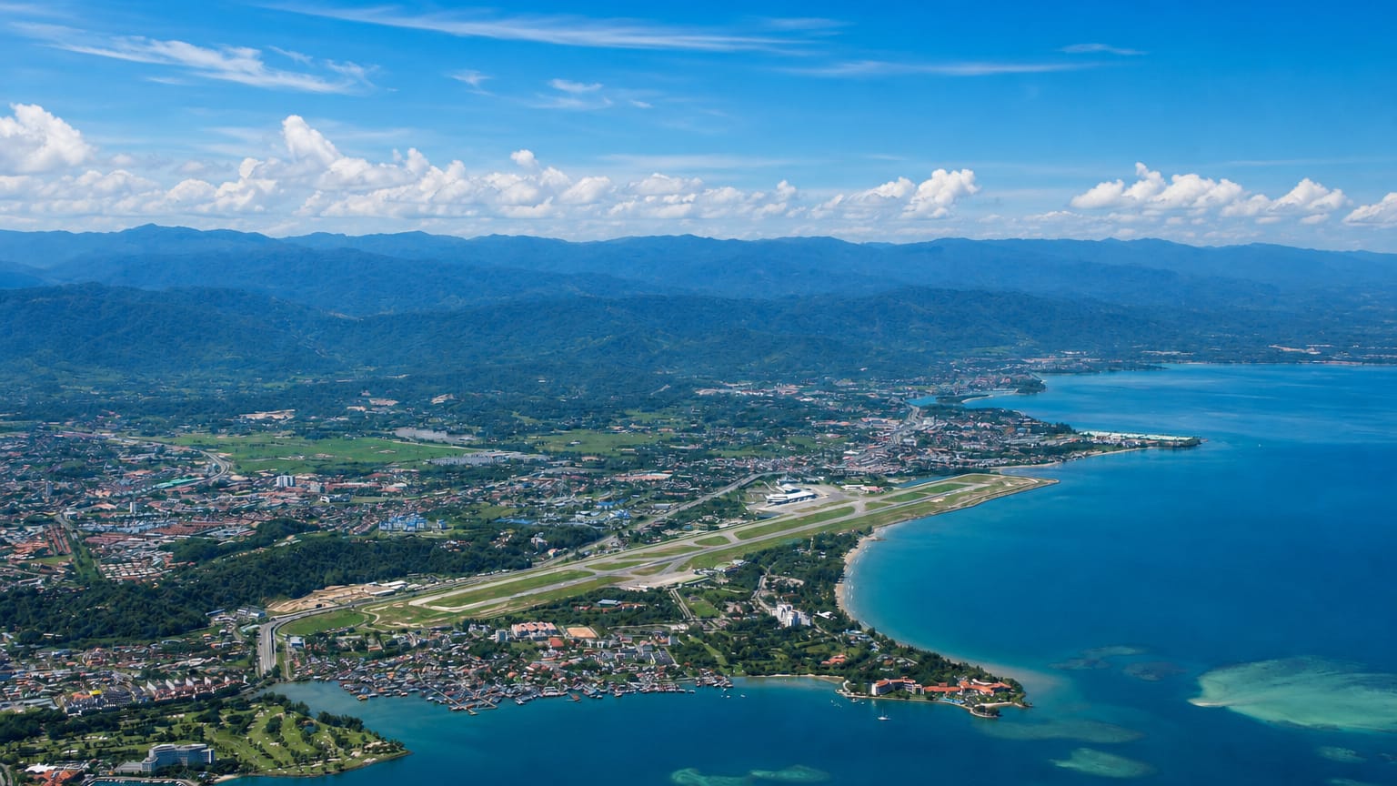 Aerial view of Kota Kinabalu's coastline, airport runway and city backed by the Crocker Range mountains
