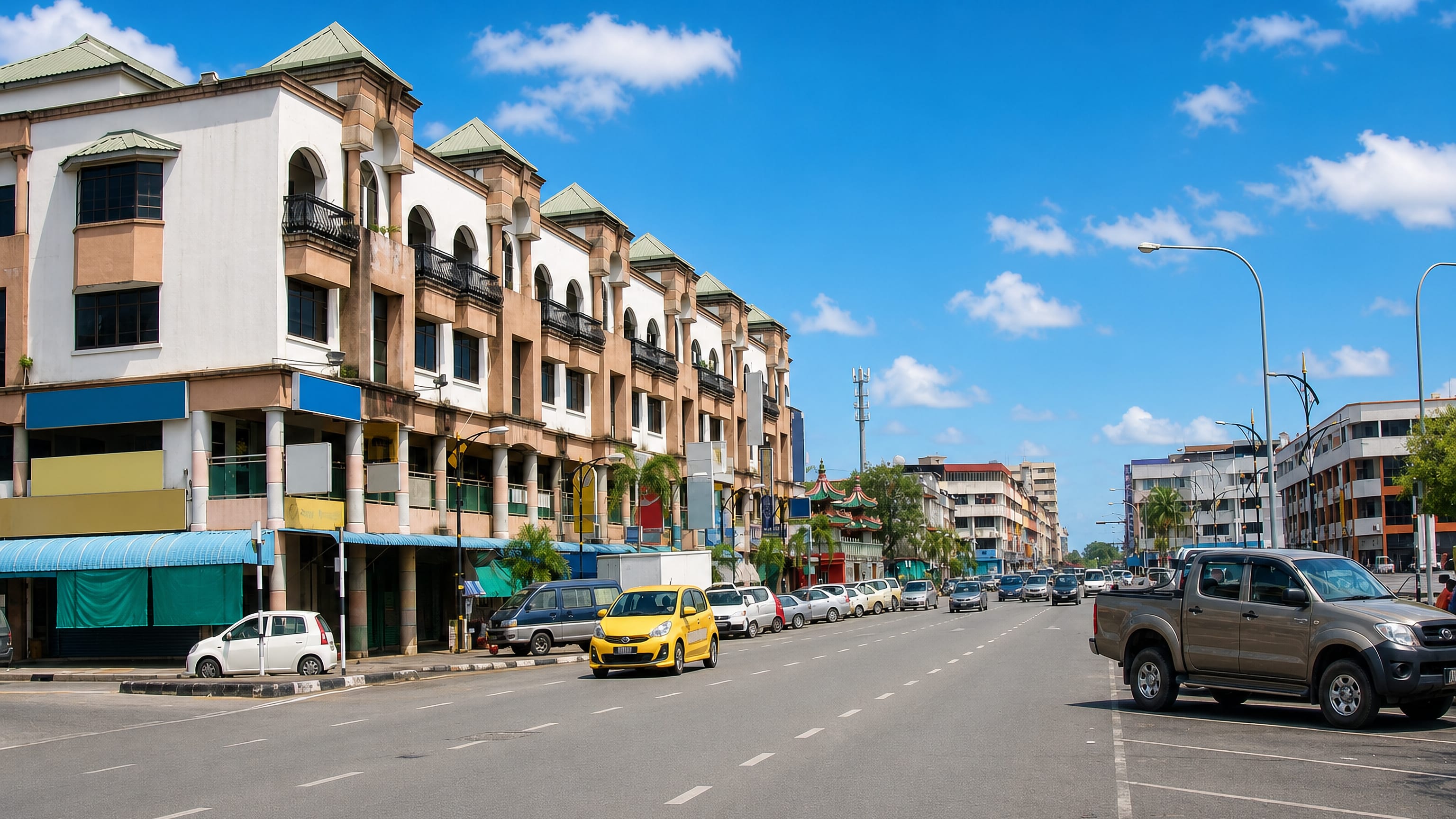 Main street through Bintulu, Sarawak, lined with shophouses and palms under a bright sky.