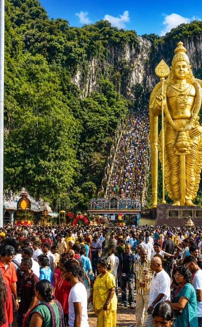 Golden Lord Murugan statue and colourful stairway at Batu Caves temple in Selangor, thronged by festival crowds.