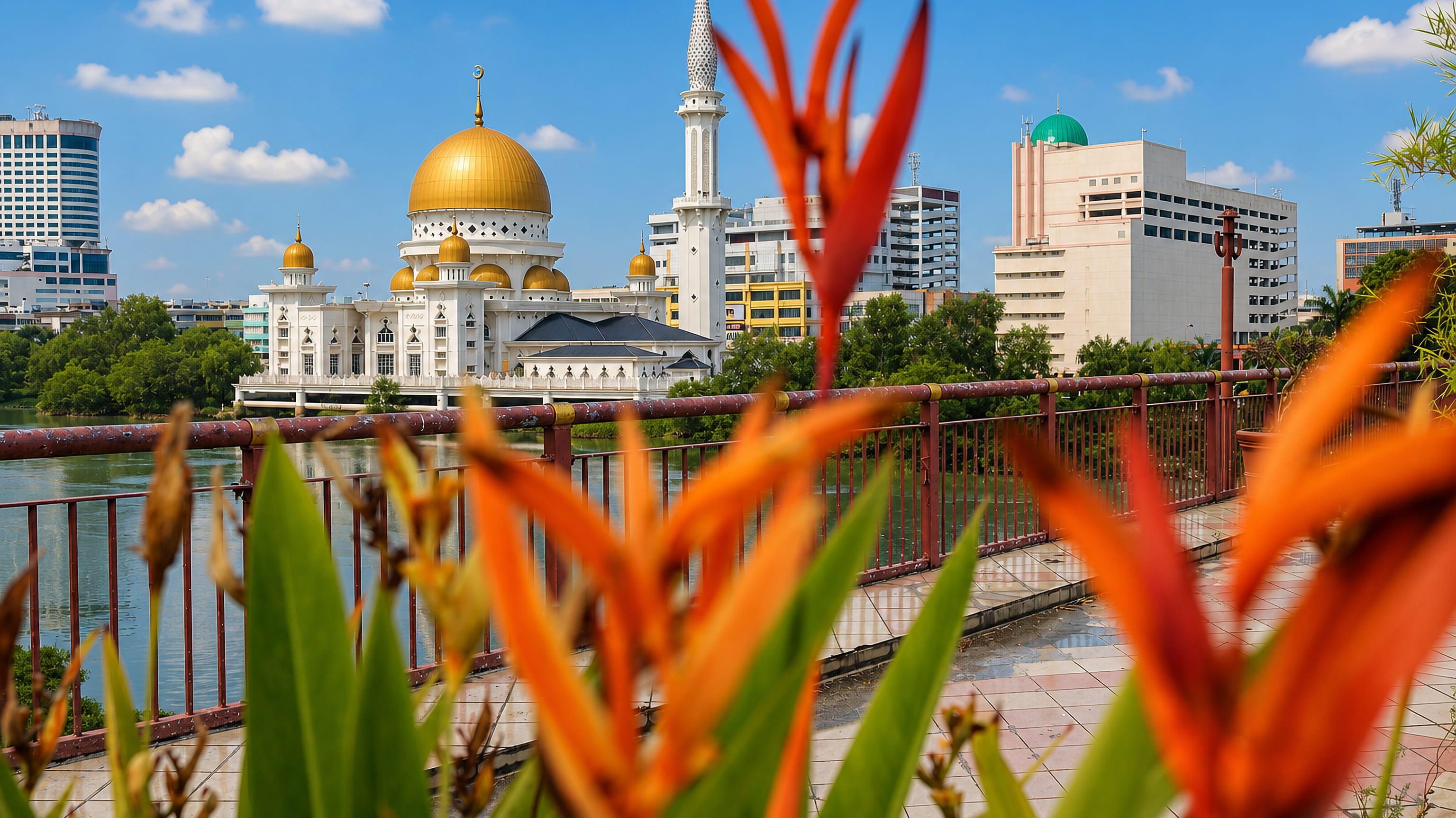 The gold-domed royal mosque on the river at Klang, Selangor, framed by riverside flowers.