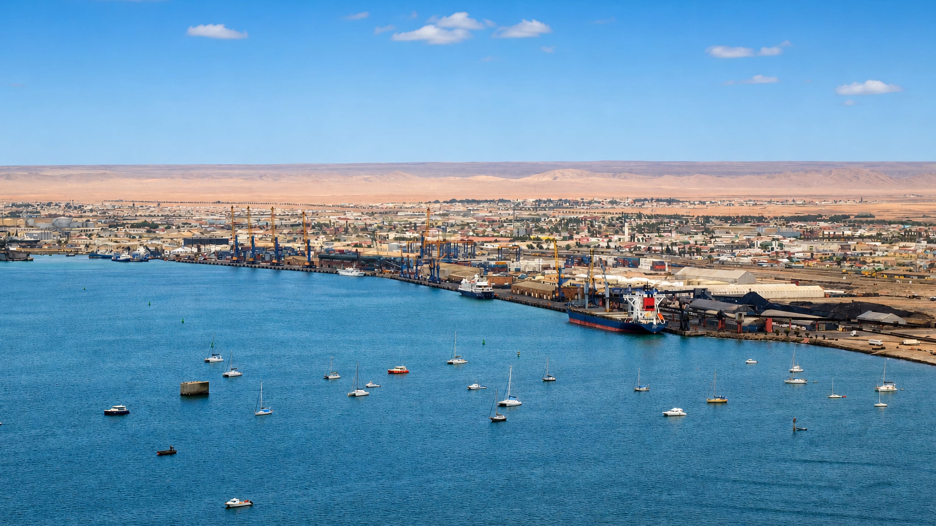 Walvis Bay's port cranes and cargo ship beside the lagoon, with yachts moored and Namib desert beyond.