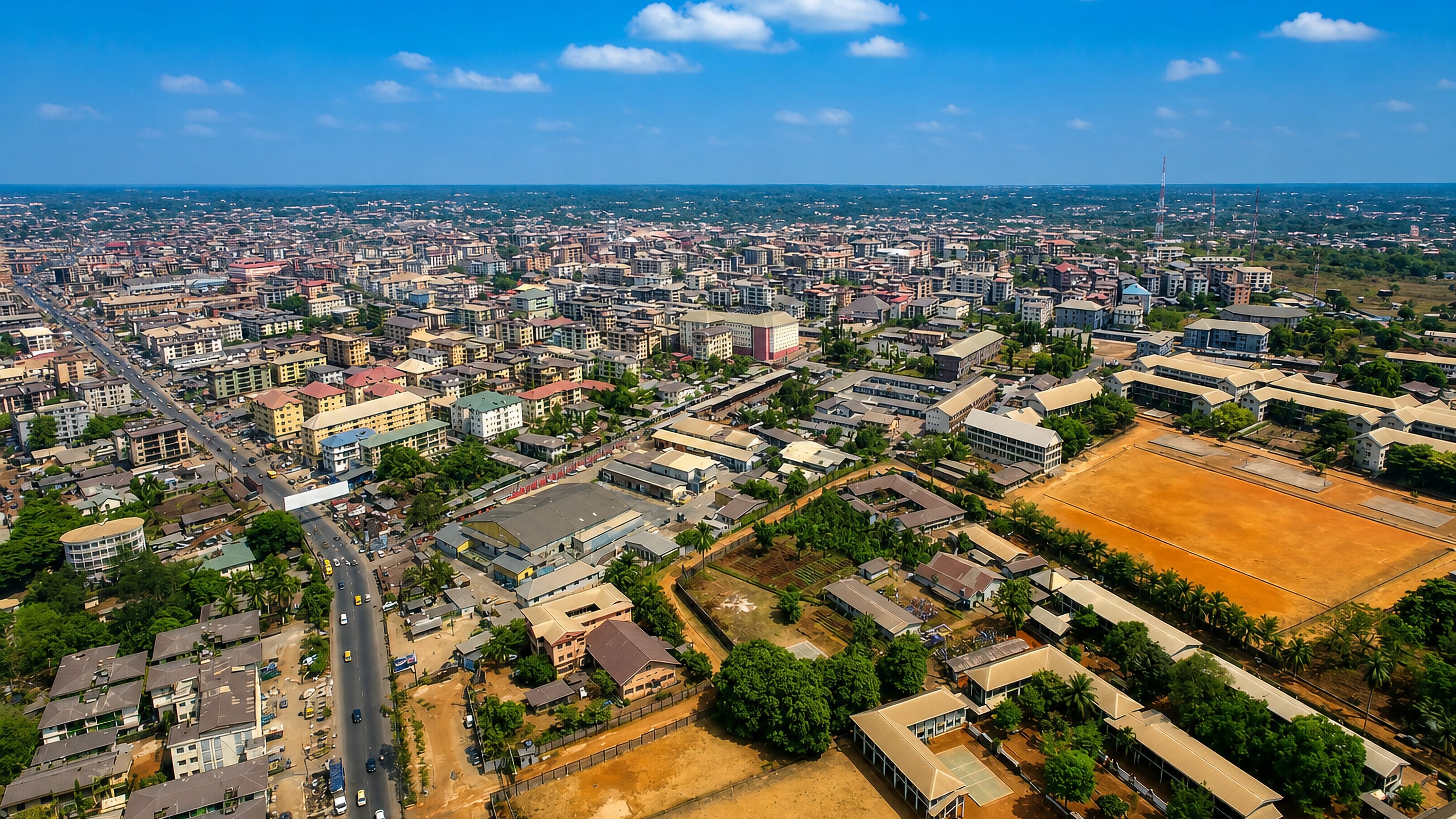 Aerial view over dense rooftops, red-earth sports fields and busy streets in Onitsha, Nigeria