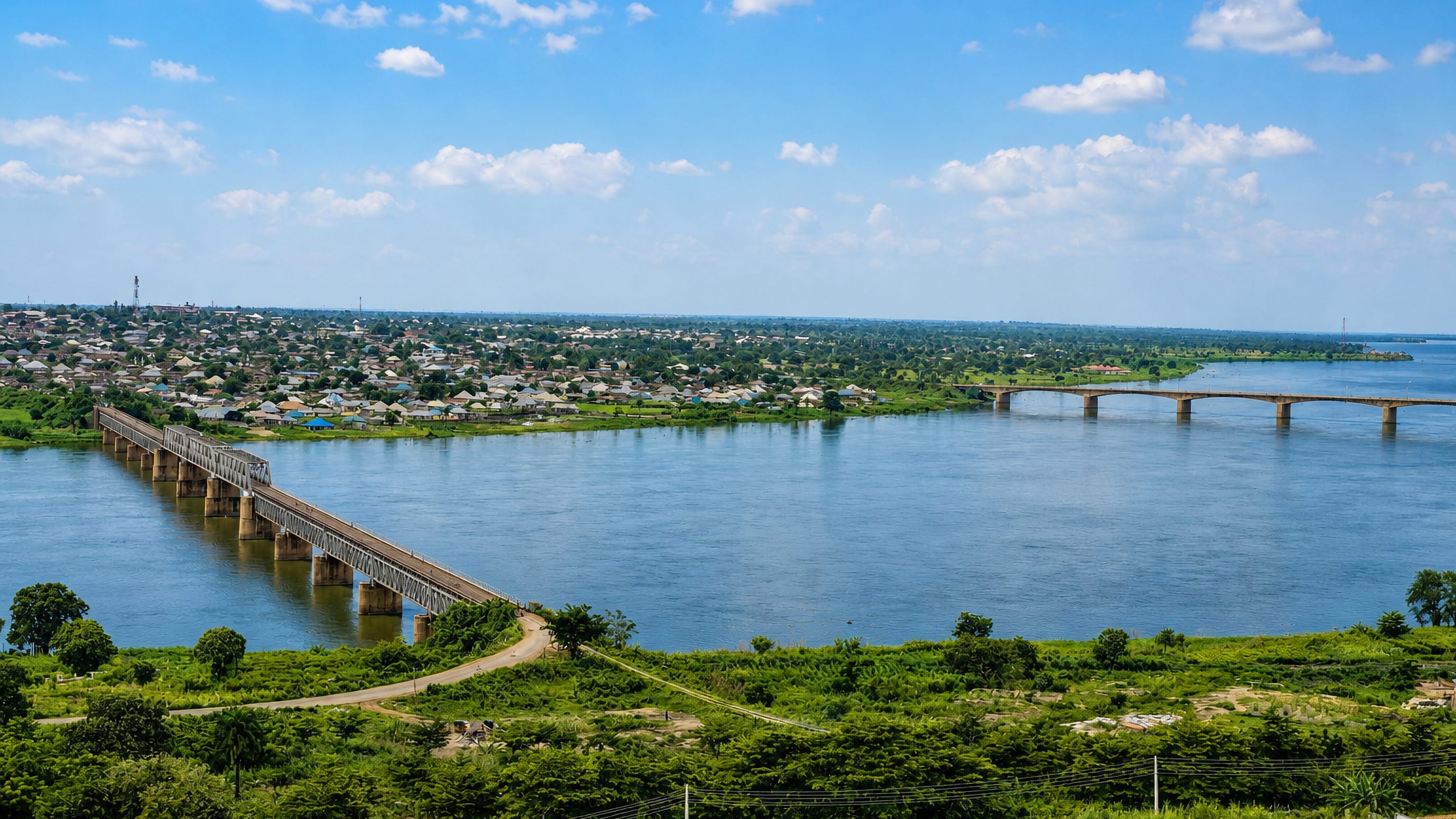 Two long bridges spanning the River Benue at Makurdi, with the town's low rooftops lining the far bank.
