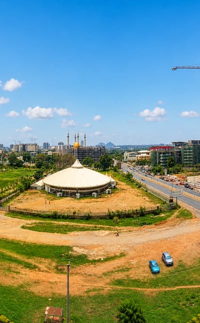 Abuja cityscape with the golden-domed National Mosque, a conical hall and high-rise towers under a blue sky.