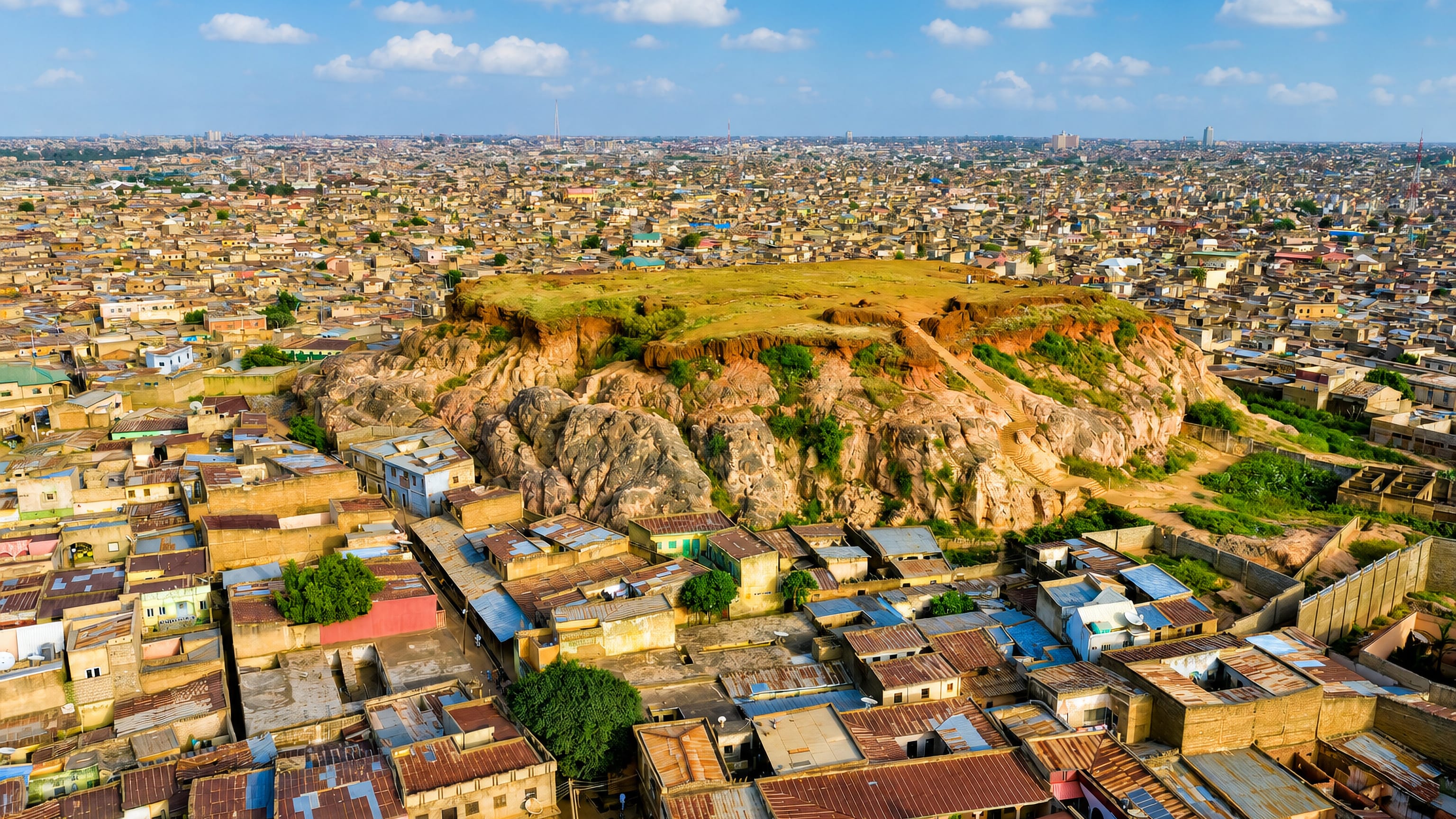 Aerial view across Kano, Nigeria, showing the dense old city of rusted metal roofs around a rocky hill