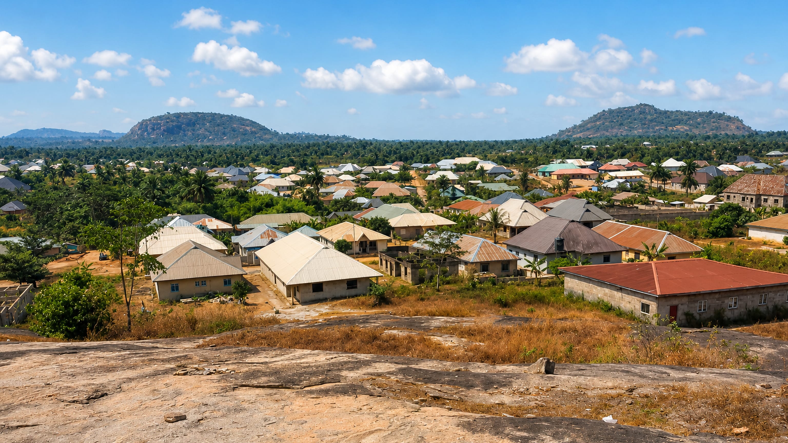 Hilltop view over Ondo, Nigeria, of metal-roofed houses spread among palms with granite hills on the horizon.