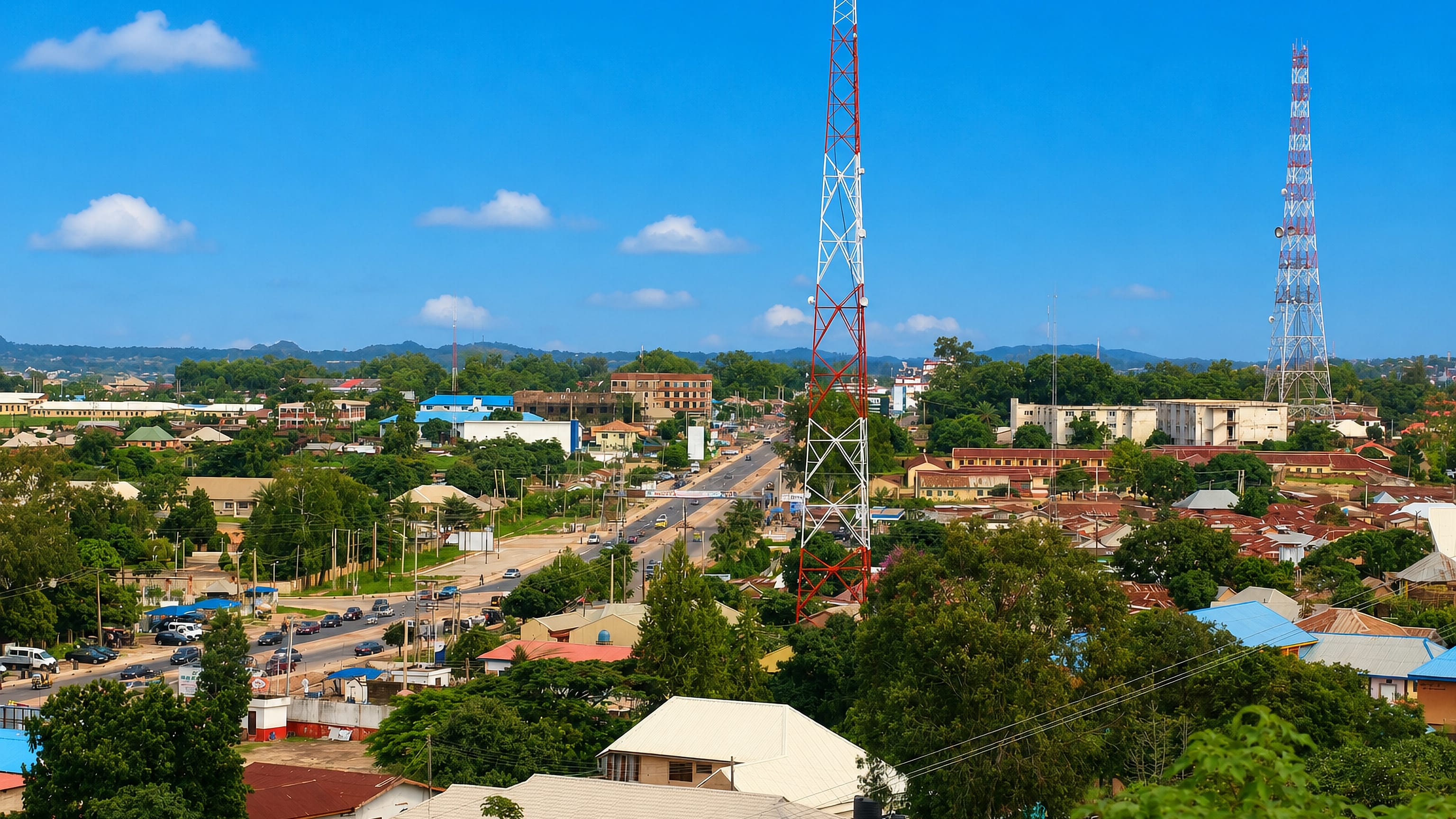 Hillside view over Jos, Nigeria, with metal roofs, telecom masts and the main road running toward distant hills.