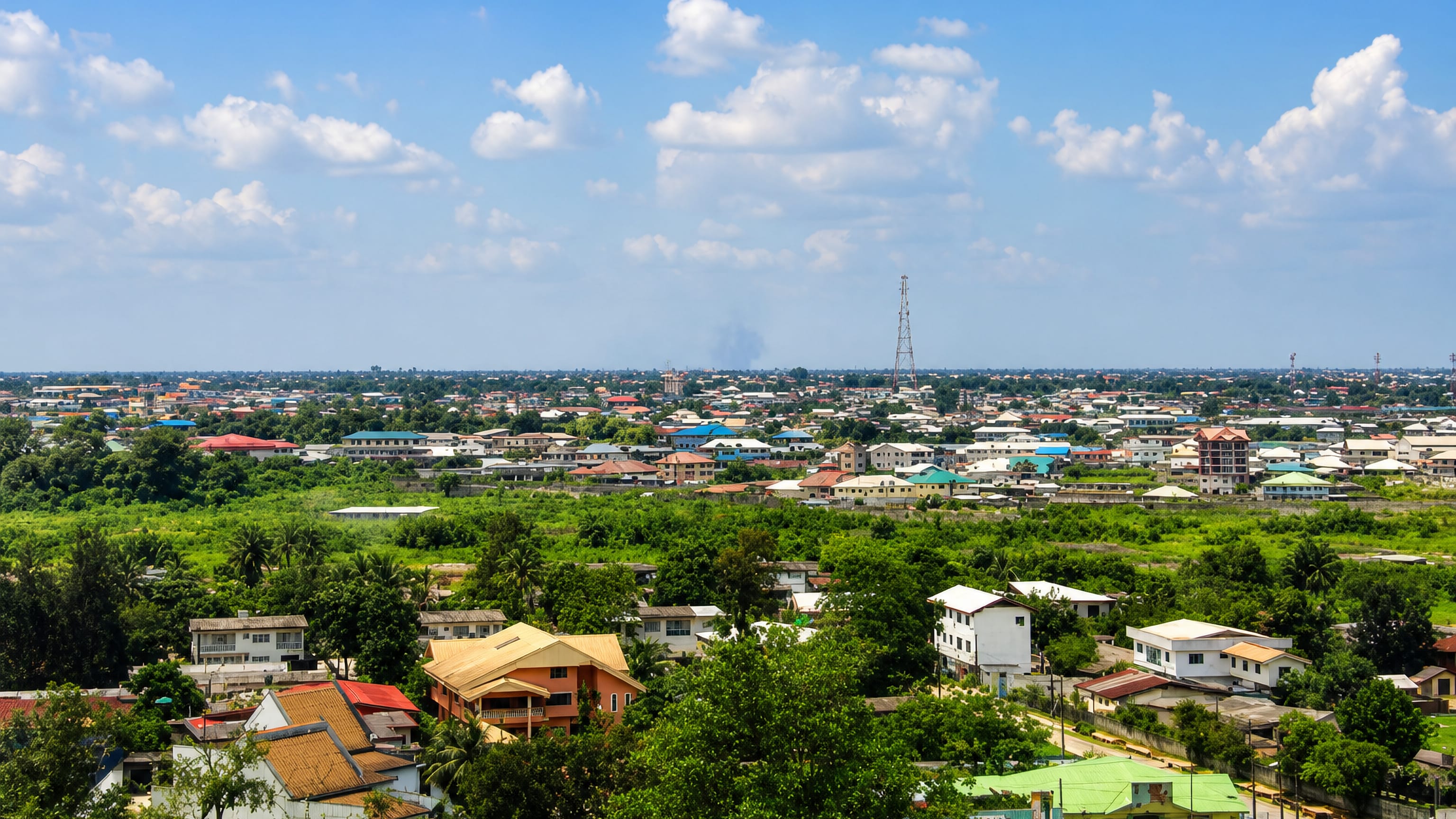 Wide daytime view over Port Harcourt, Nigeria, low-rise homes and palm-lined greenery under a blue sky.