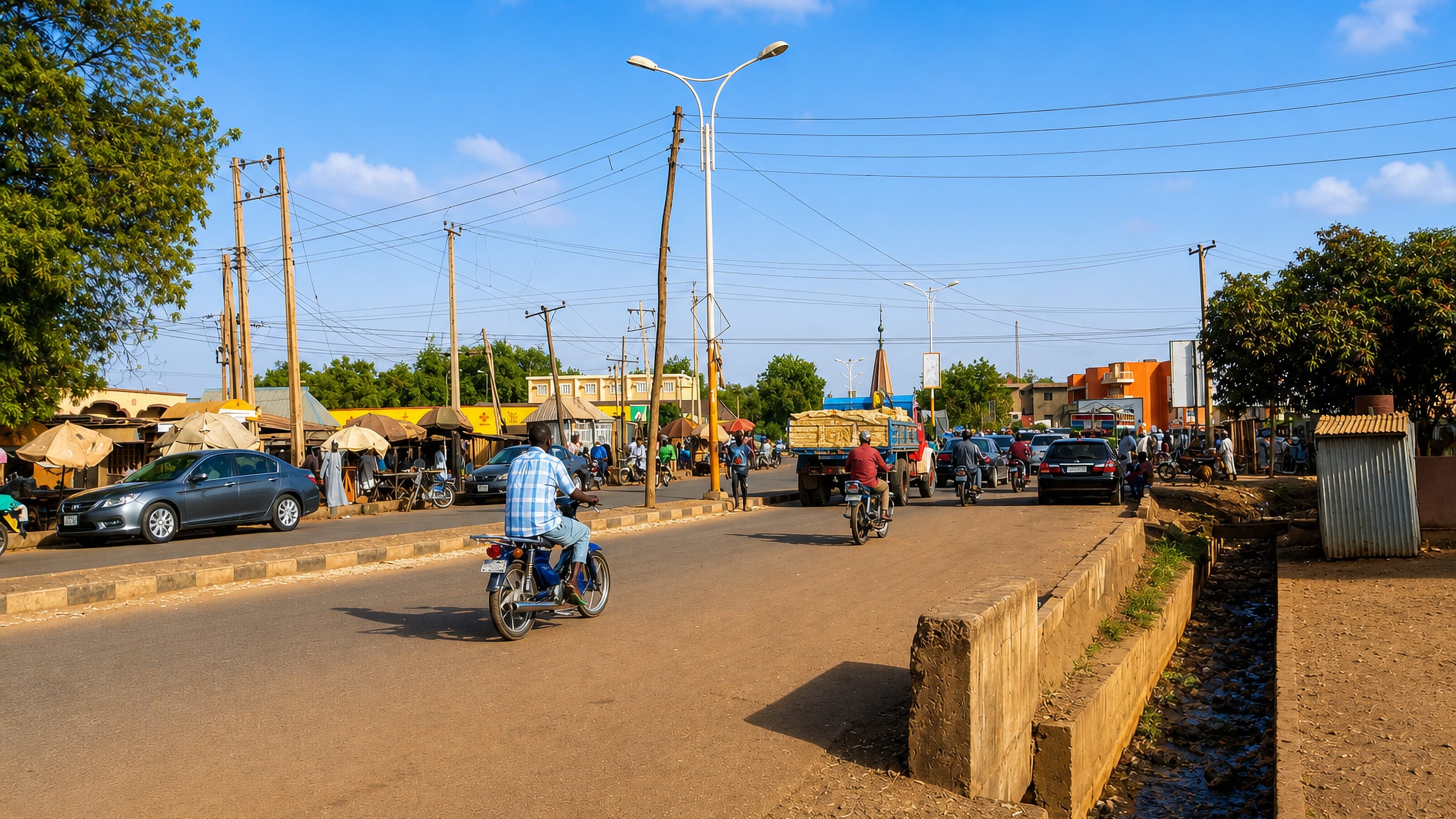 A busy Sokoto street with motorcycles, roadside market stalls and a minaret rising beyond.