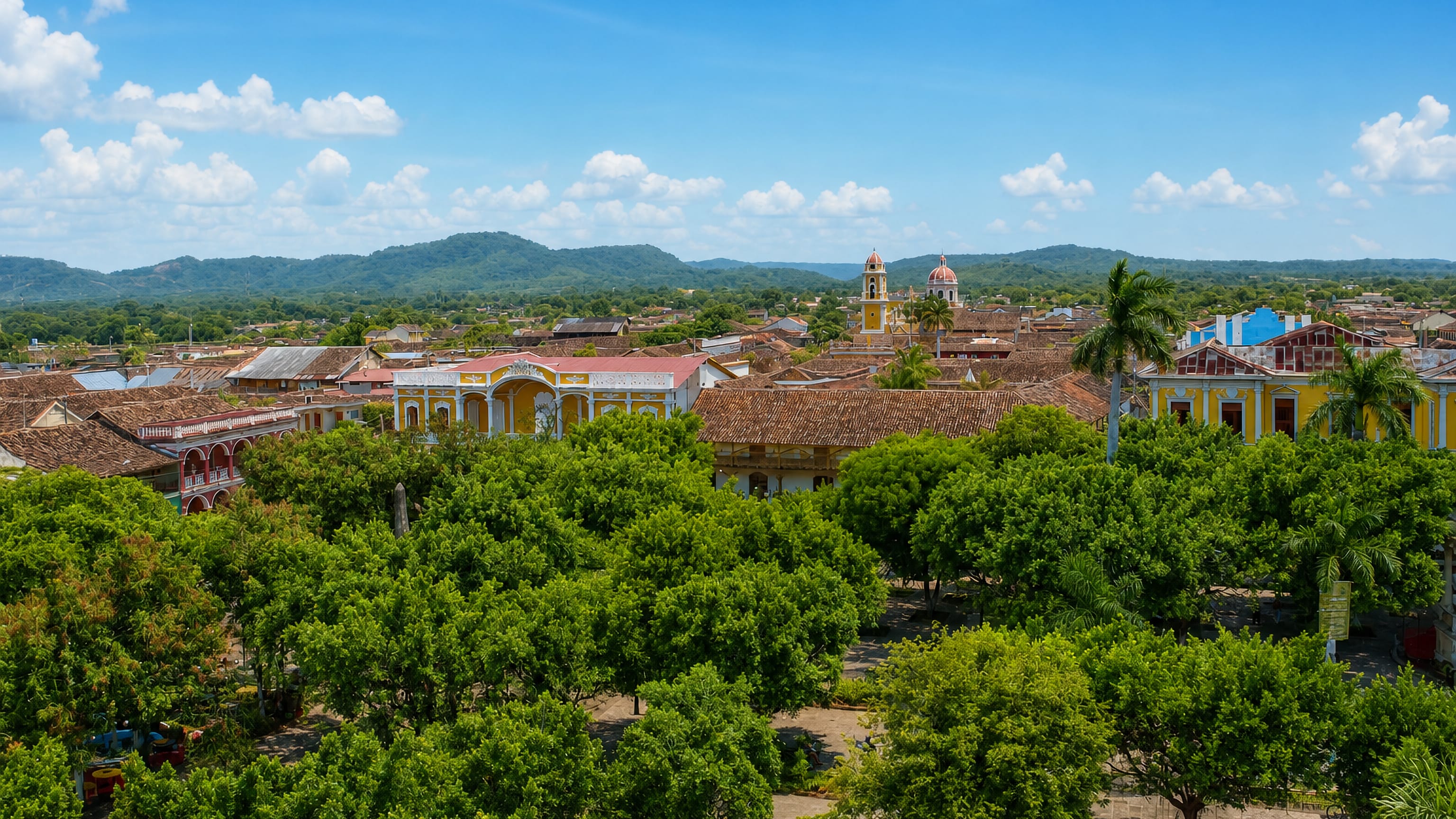 Terracotta rooftops, colourful colonial facades and church towers of Granada, Nicaragua, above a tree-filled plaza.