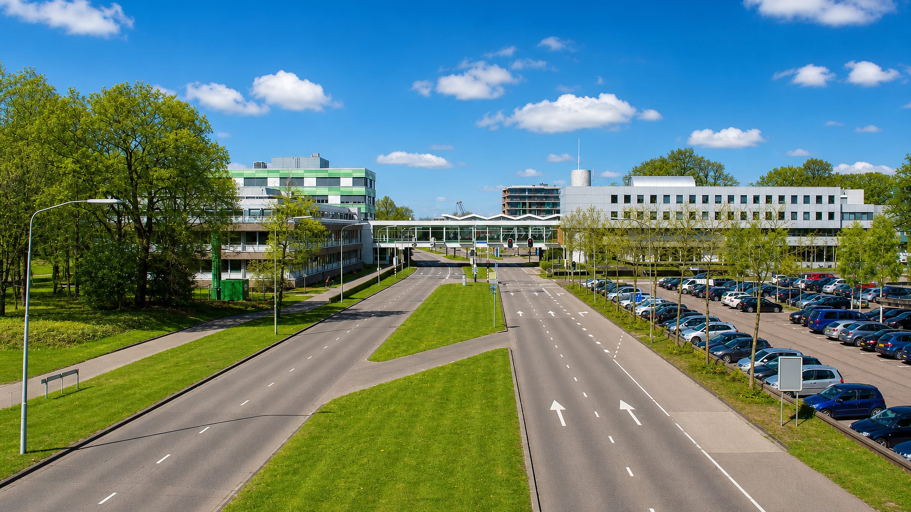 Modern low-rise offices, a wide empty road and parking among spring greenery in Emmen, Netherlands.