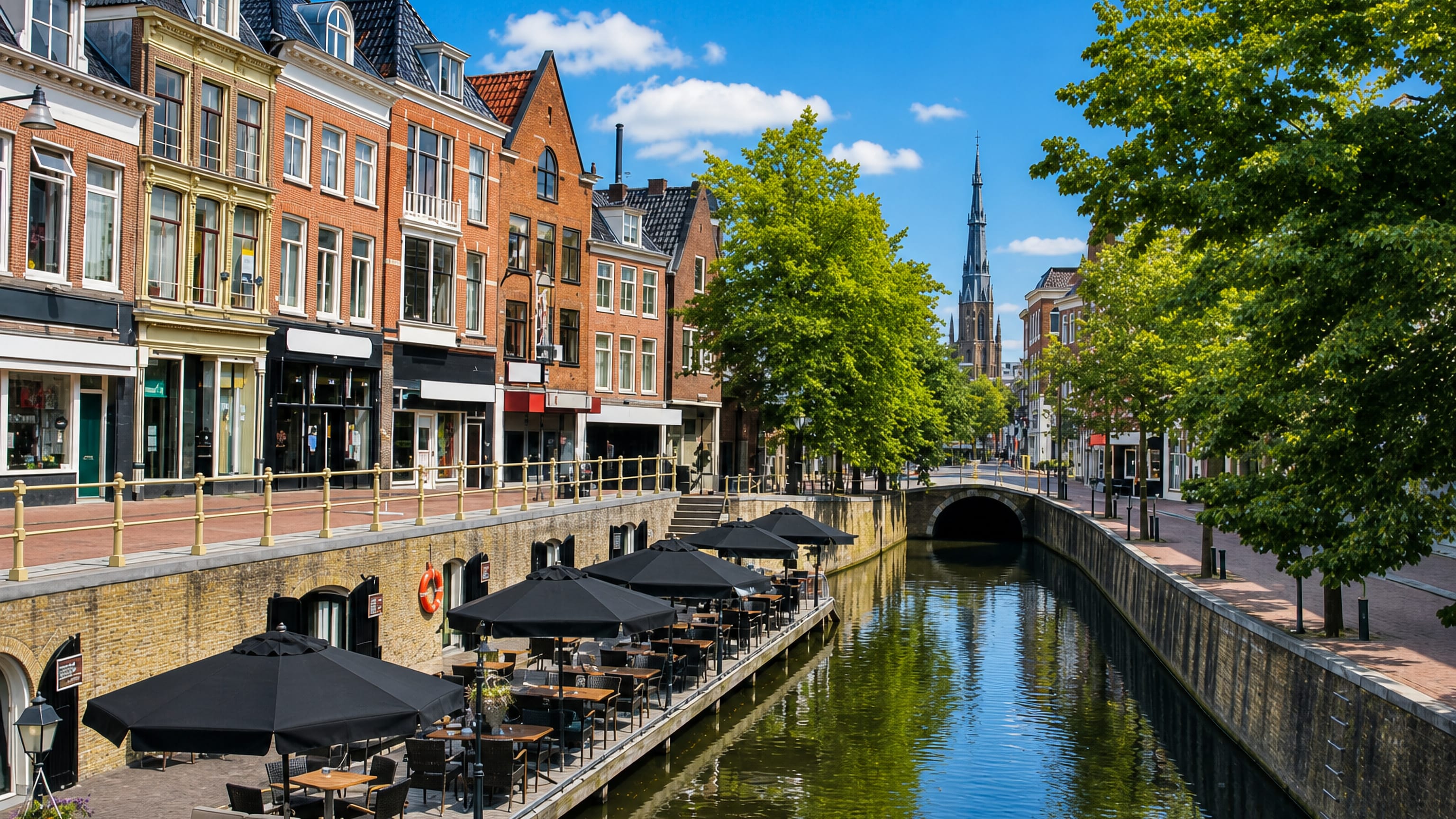 Canalside cafe terrace and brick gabled houses in central Leeuwarden, with a tall church spire beyond