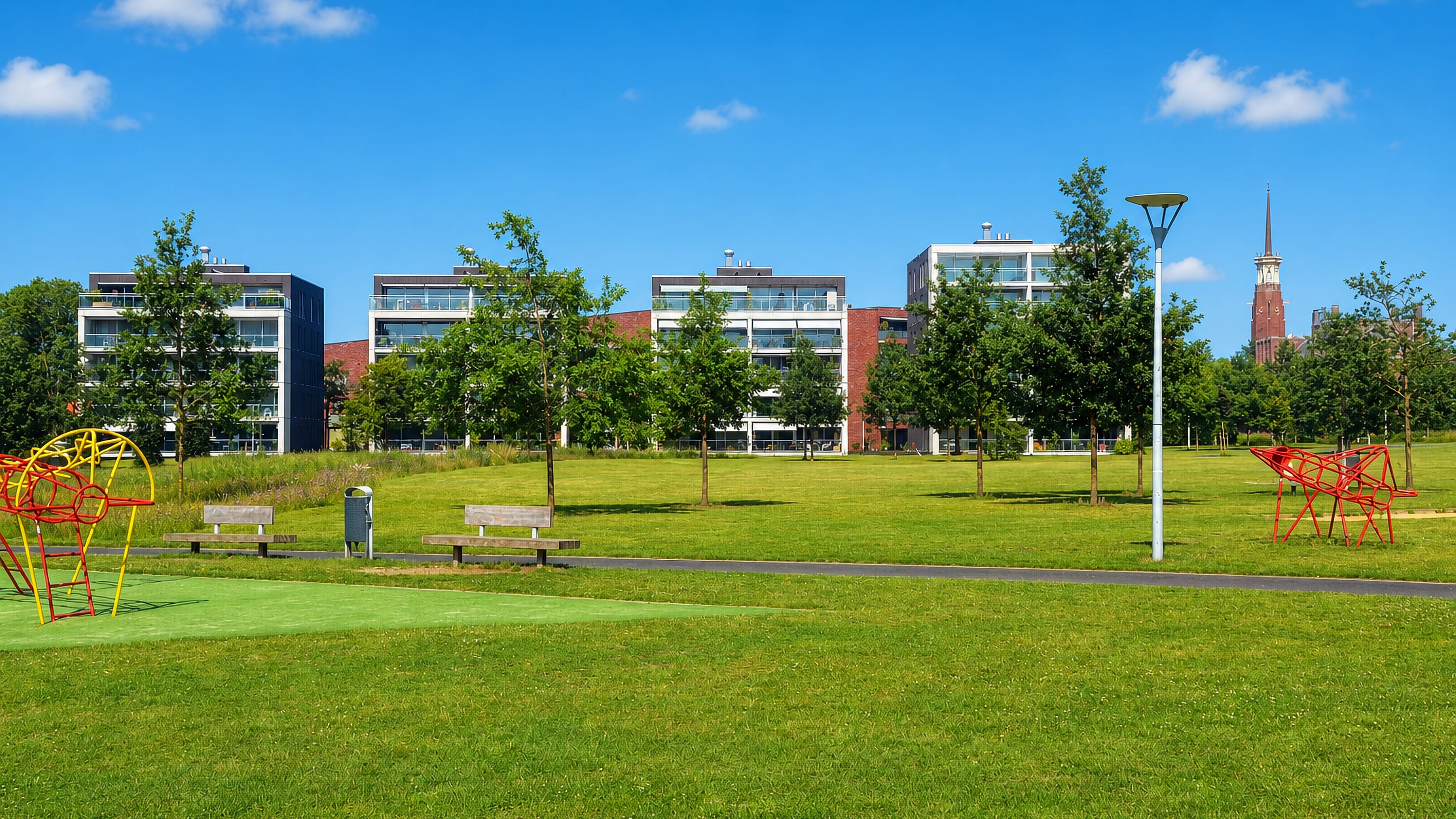 Modern apartment blocks and a church spire beyond an open park lawn at Hengstdal, Nijmegen