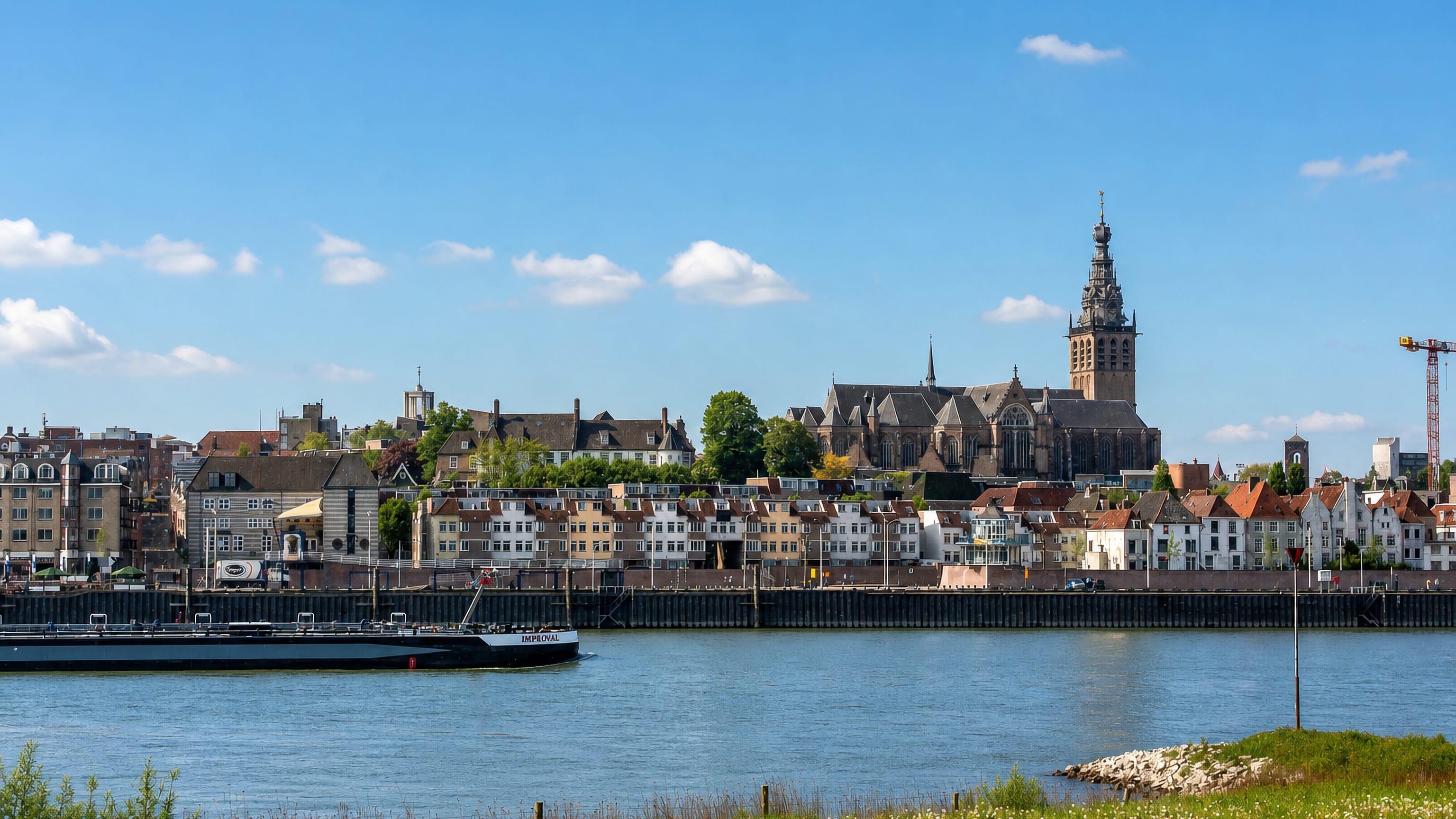 Nijmegen's Waal riverfront with the Stevenskerk tower above quayside houses and a barge passing