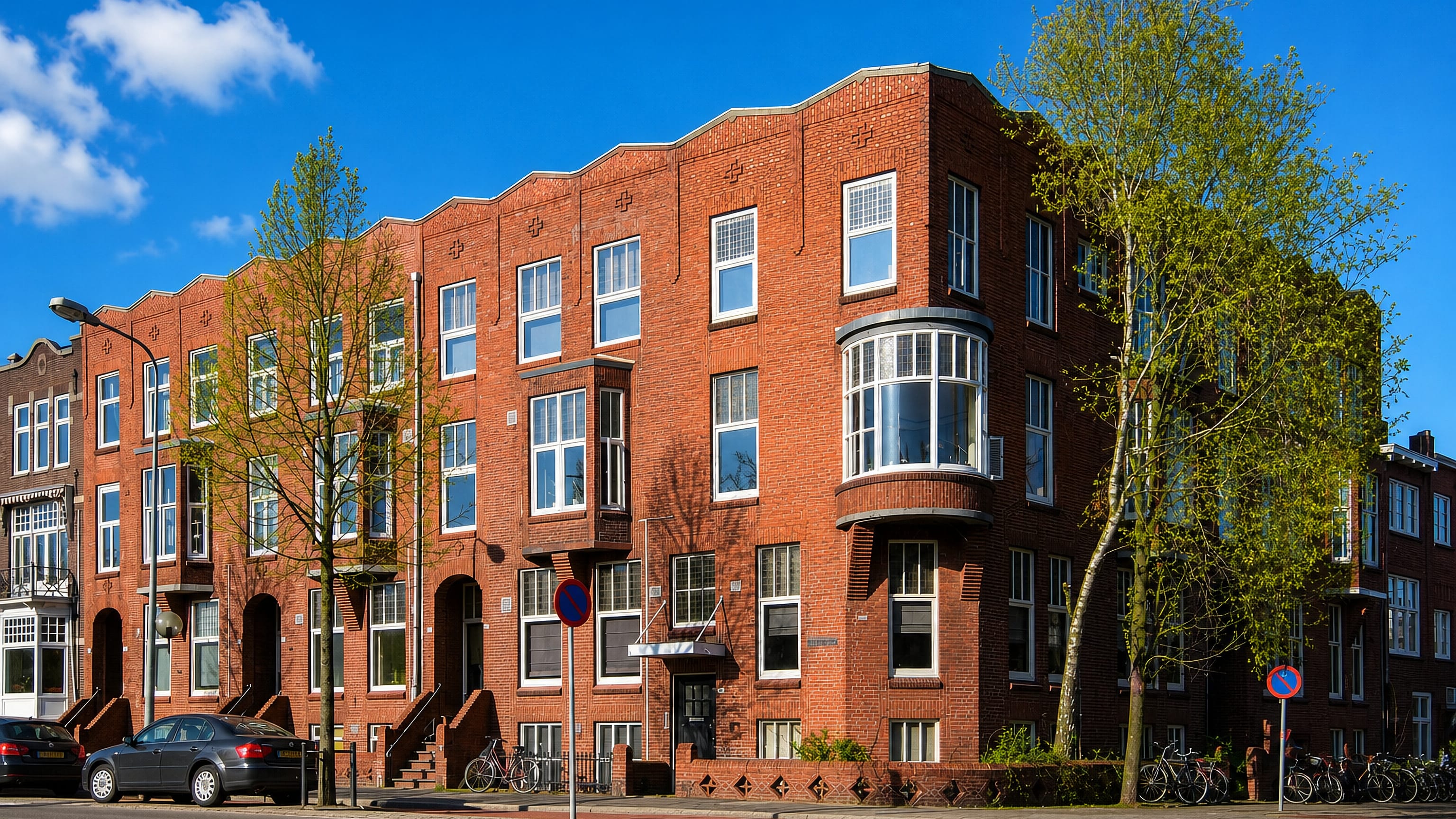 Amsterdam School brick apartment blocks with bay windows lining a quiet street in Helpman, Groningen.