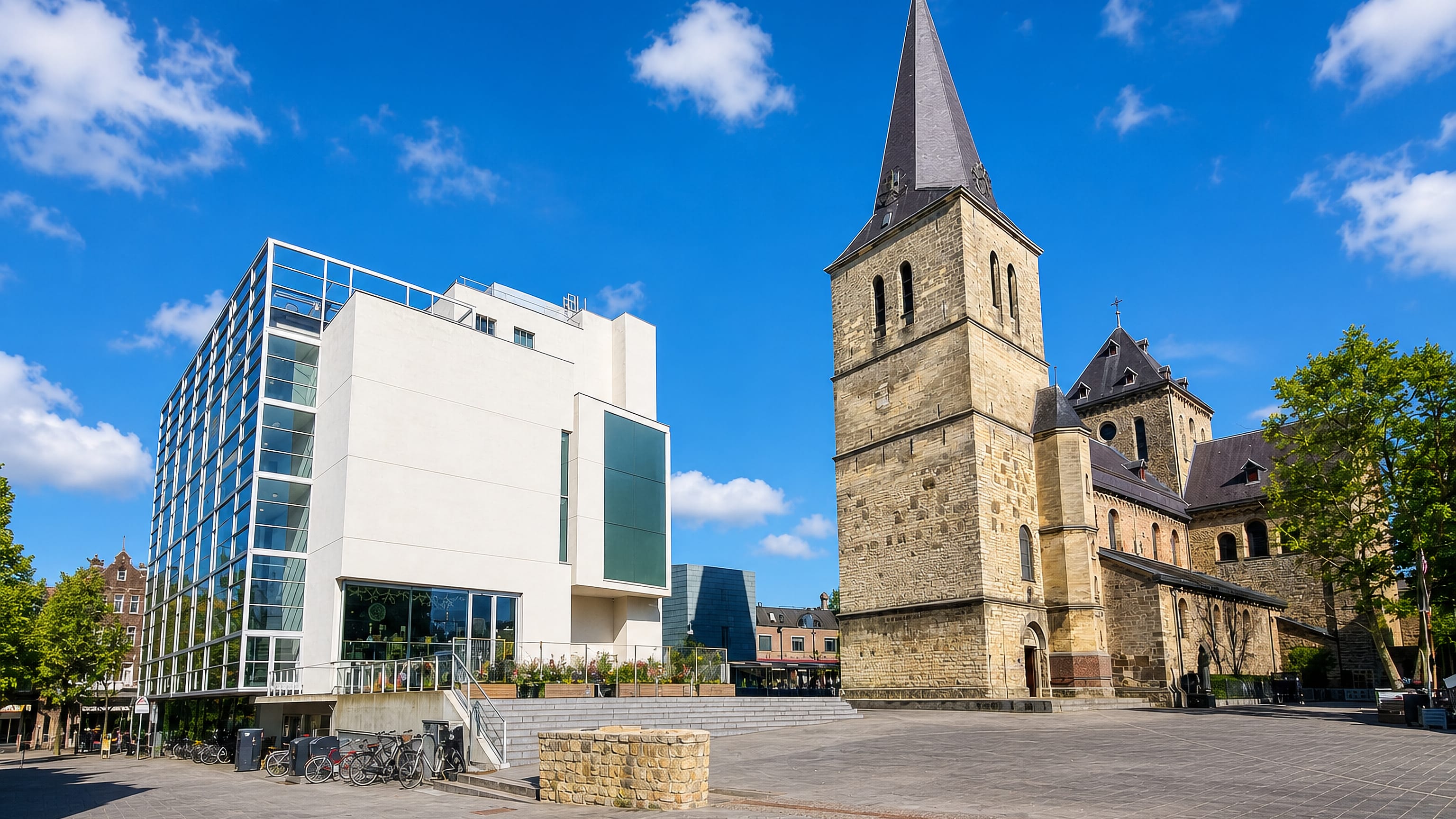 Heerlen's Pancratiusplein with the stone tower of the Pancratius church beside a modern glass-fronted building.