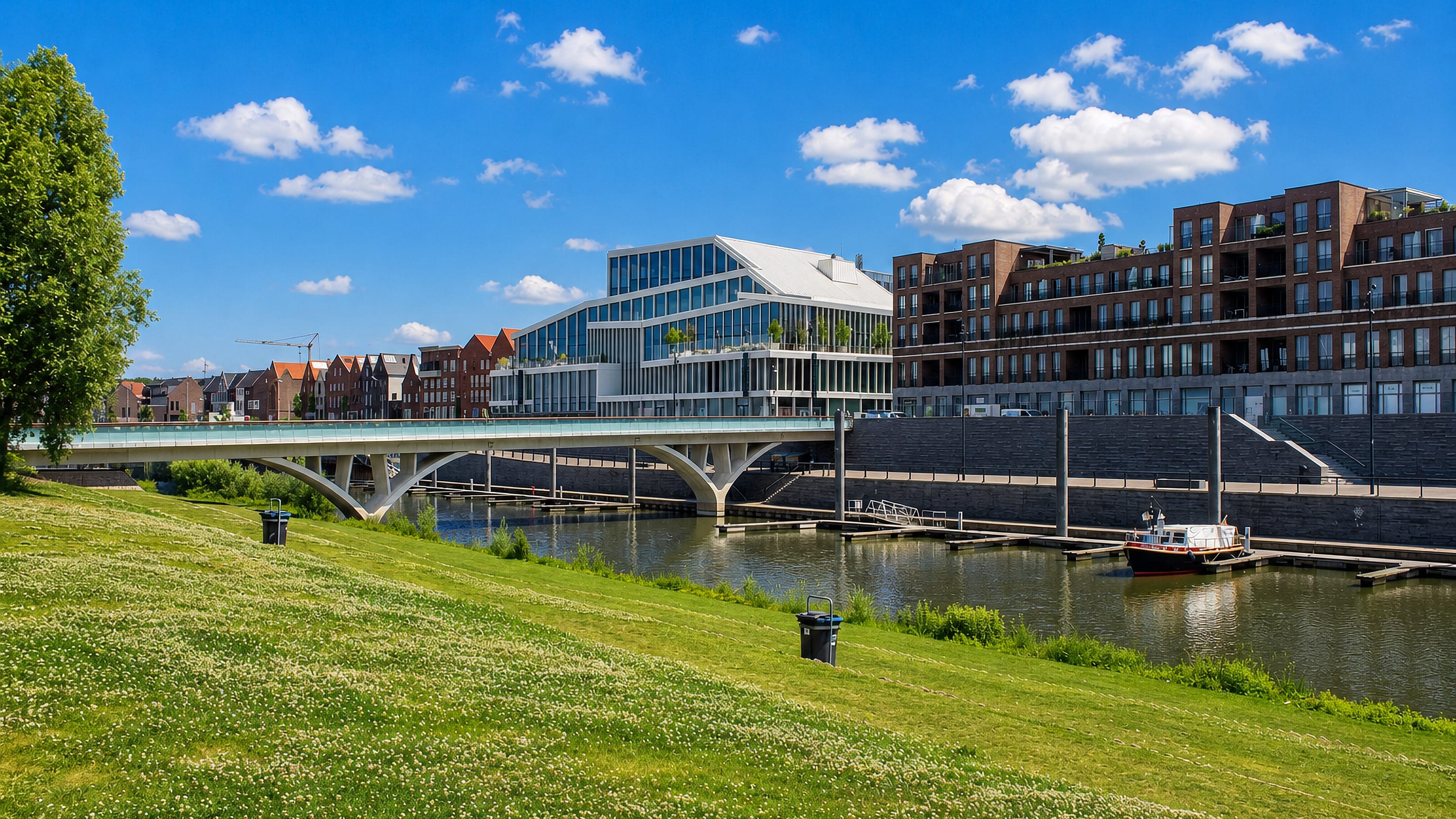 River quay in Venlo, Netherlands, with a modern glass office block, brick apartments and a bridge.