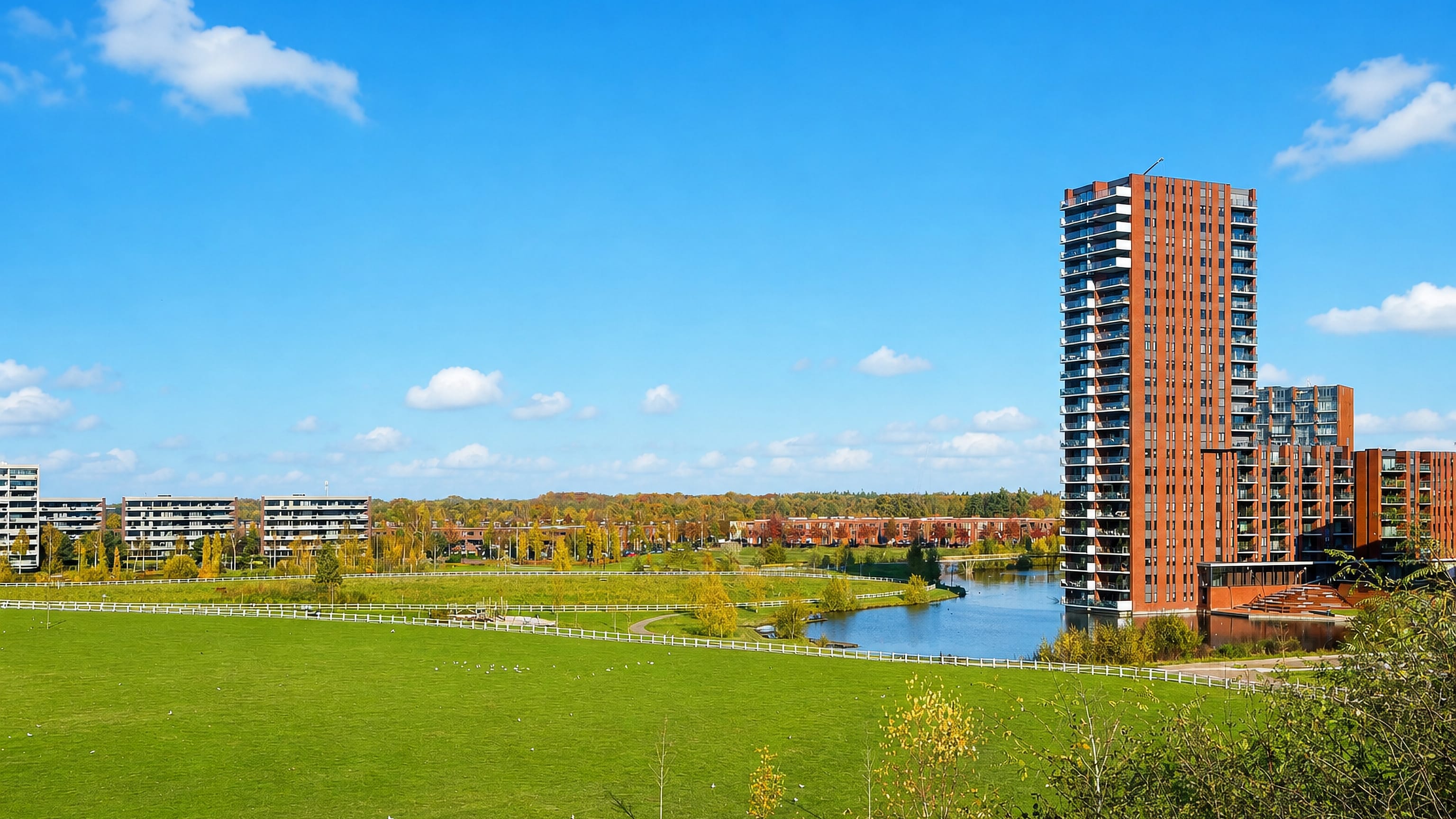 Strijp's red-brick residential tower above a waterside park and open meadow in western Eindhoven