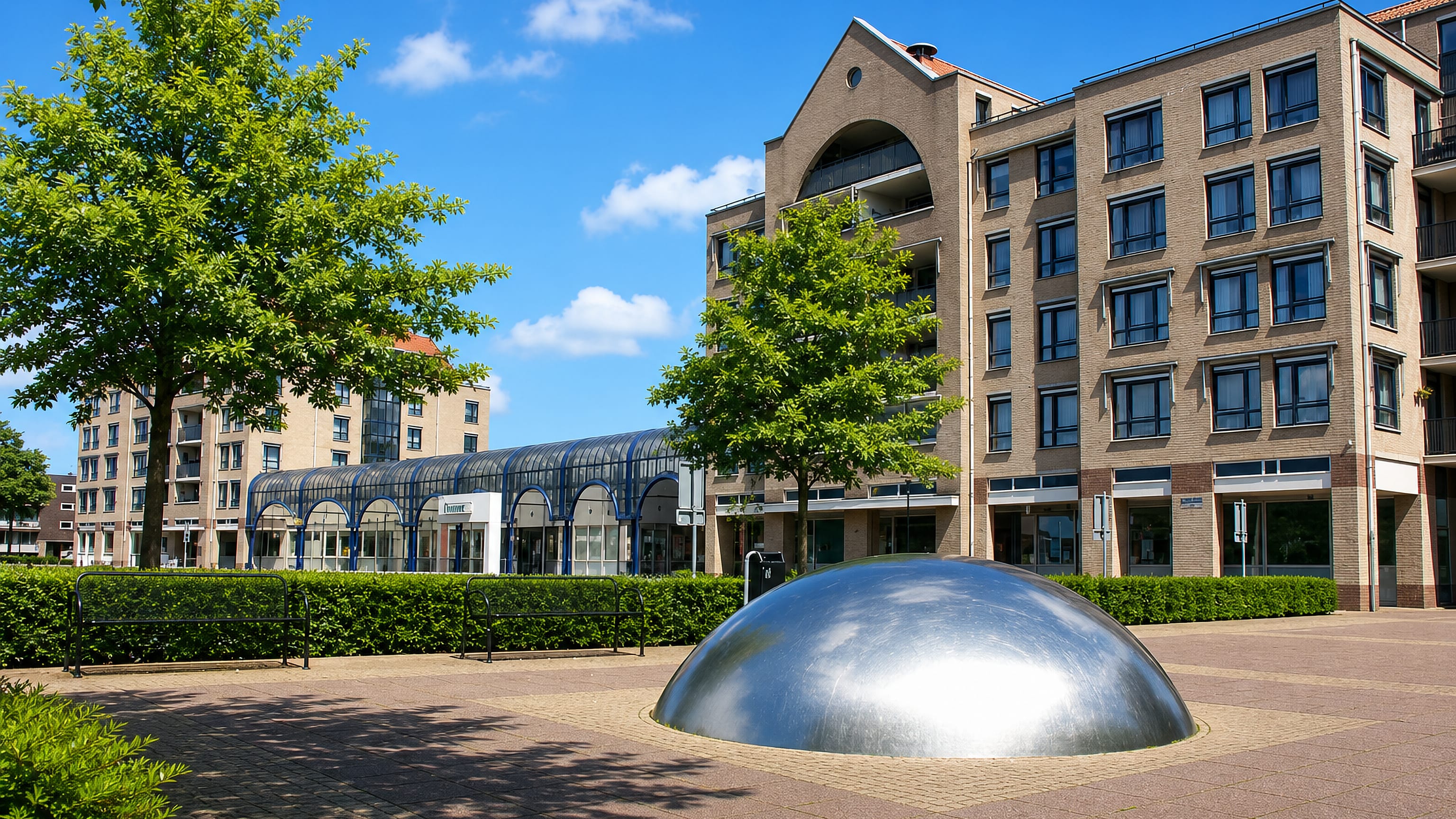 A brick-paved square in Oss, Netherlands, with a glazed shopping arcade, apartment blocks and a steel dome sculpture.