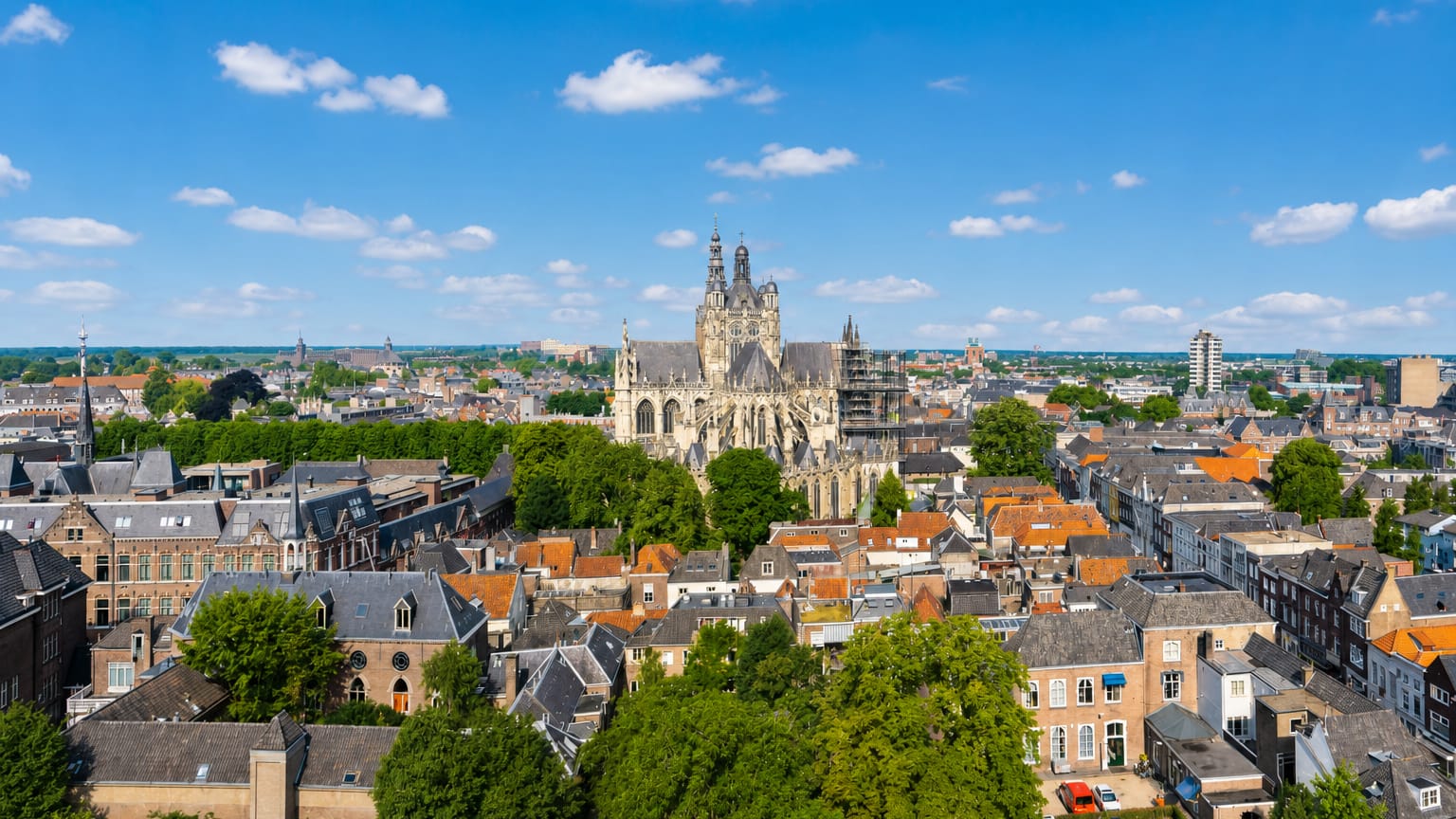 St. John's Cathedral rising above the historic rooftops of 's-Hertogenbosch under a blue sky.