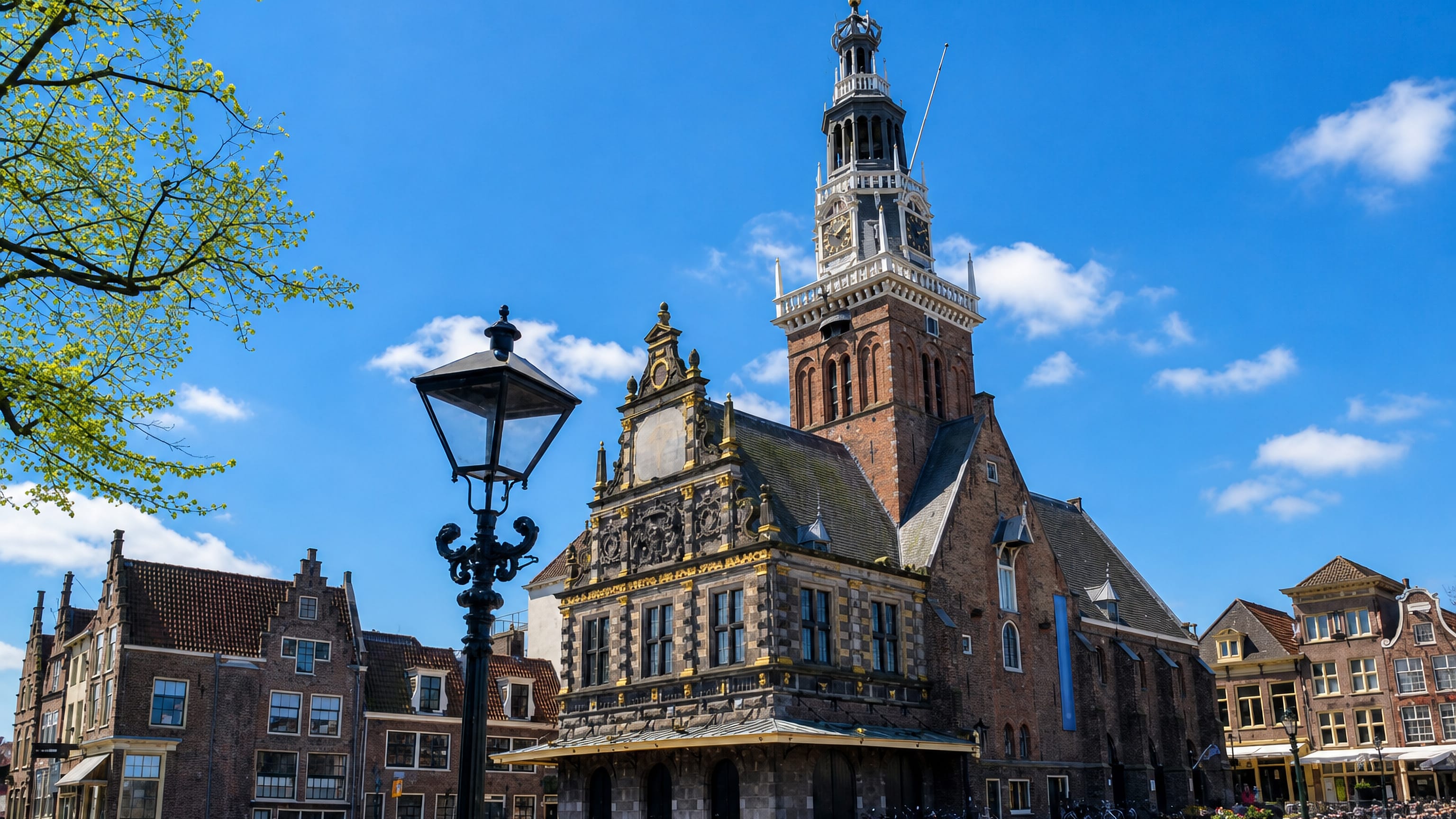 Alkmaar's Waag weigh house and its clock tower rising over the brick-paved Waagplein under a blue sky.