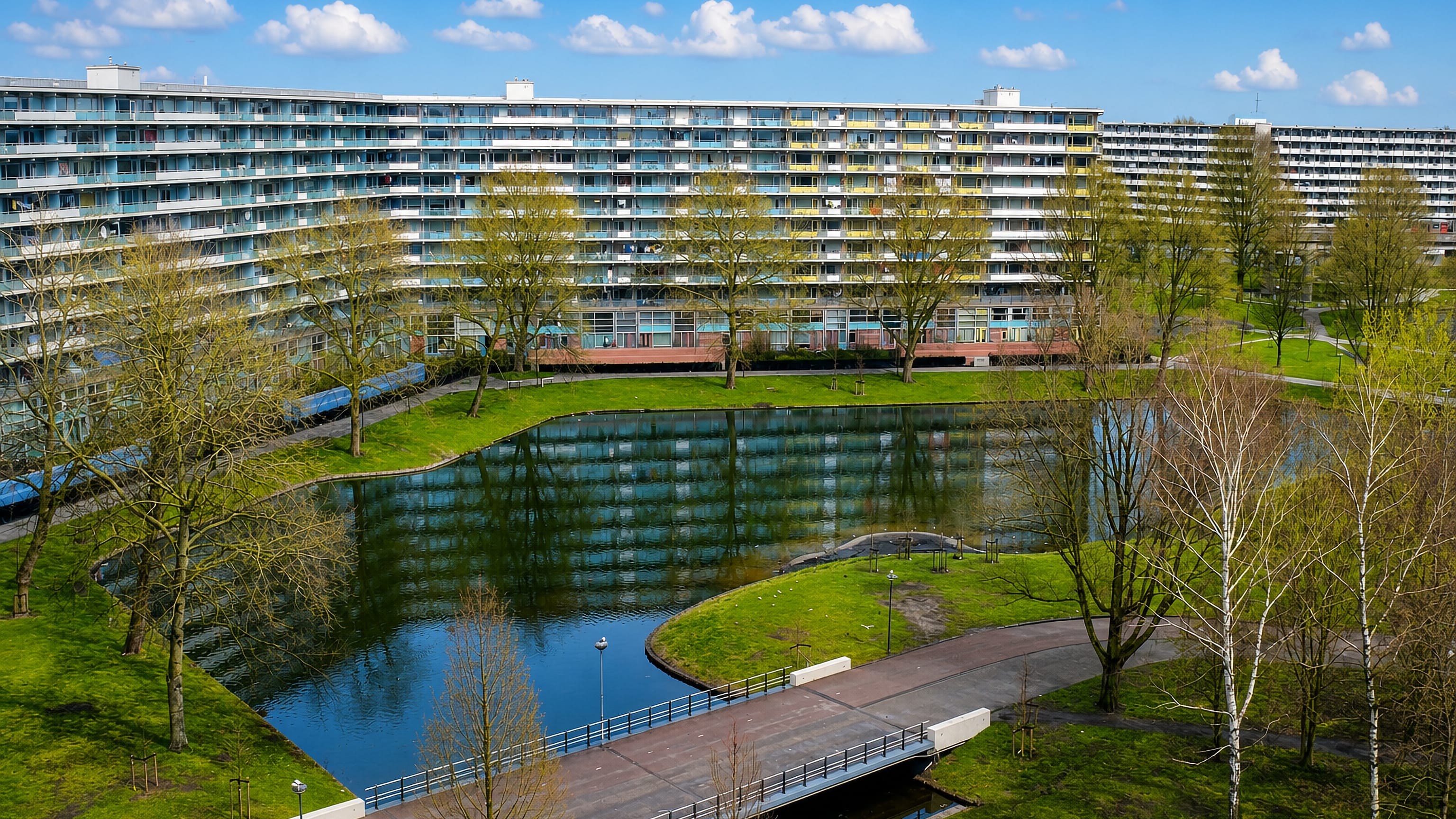 Curving honeycomb apartment slabs of Bijlmermeer reflected in a landscaped canal in Amsterdam Zuidoost