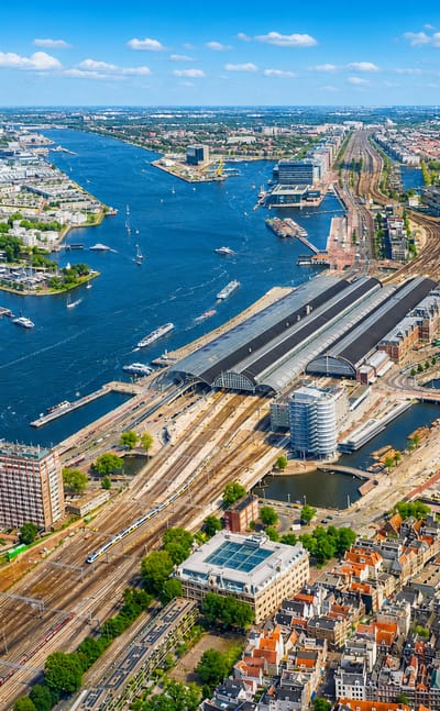 Aerial view of Amsterdam's Centraal Station and the IJ waterfront with canals and rooftops