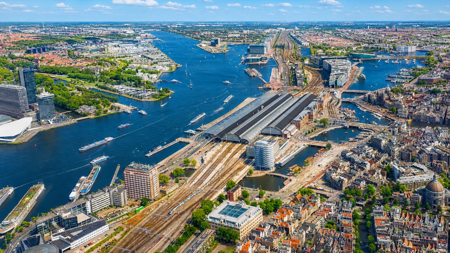Aerial view of Amsterdam's Centraal Station and the IJ waterfront with canals and rooftops